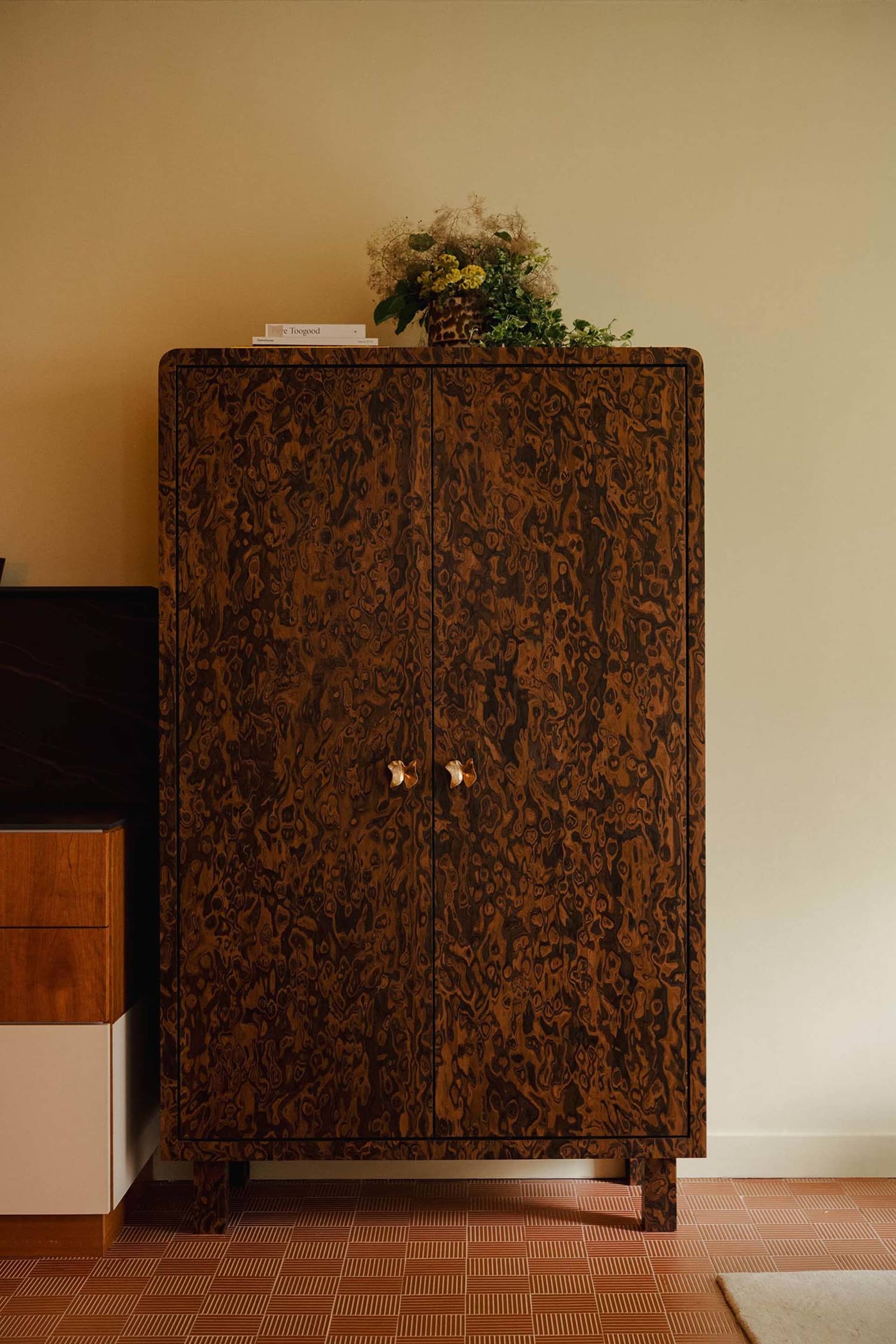 A modern living room with a wooden storage unit featuring two doors with gold handles, a vase of flowers on top, and a checke