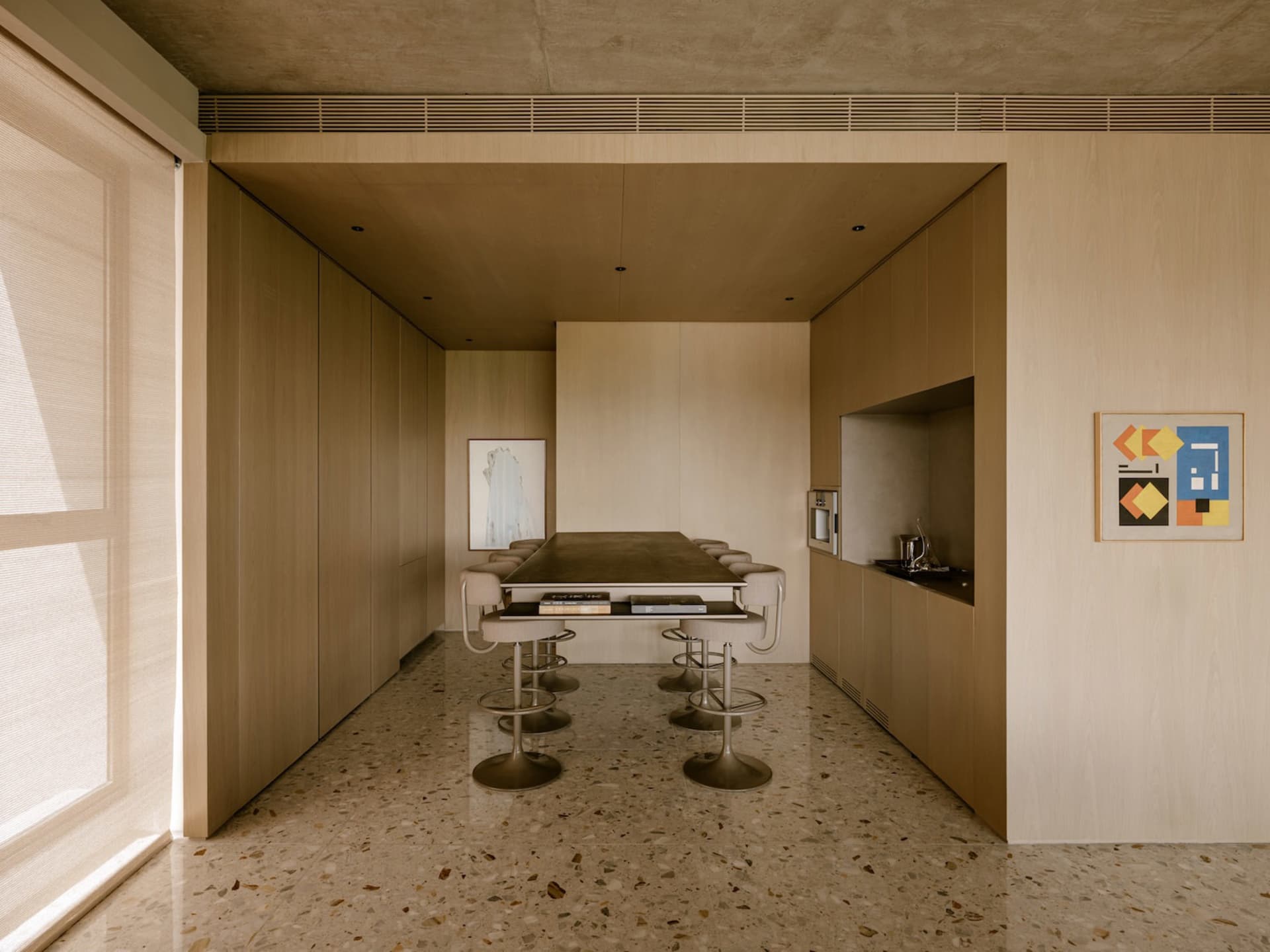 A modern kitchen with wood-paneled walls and a long table with stools.