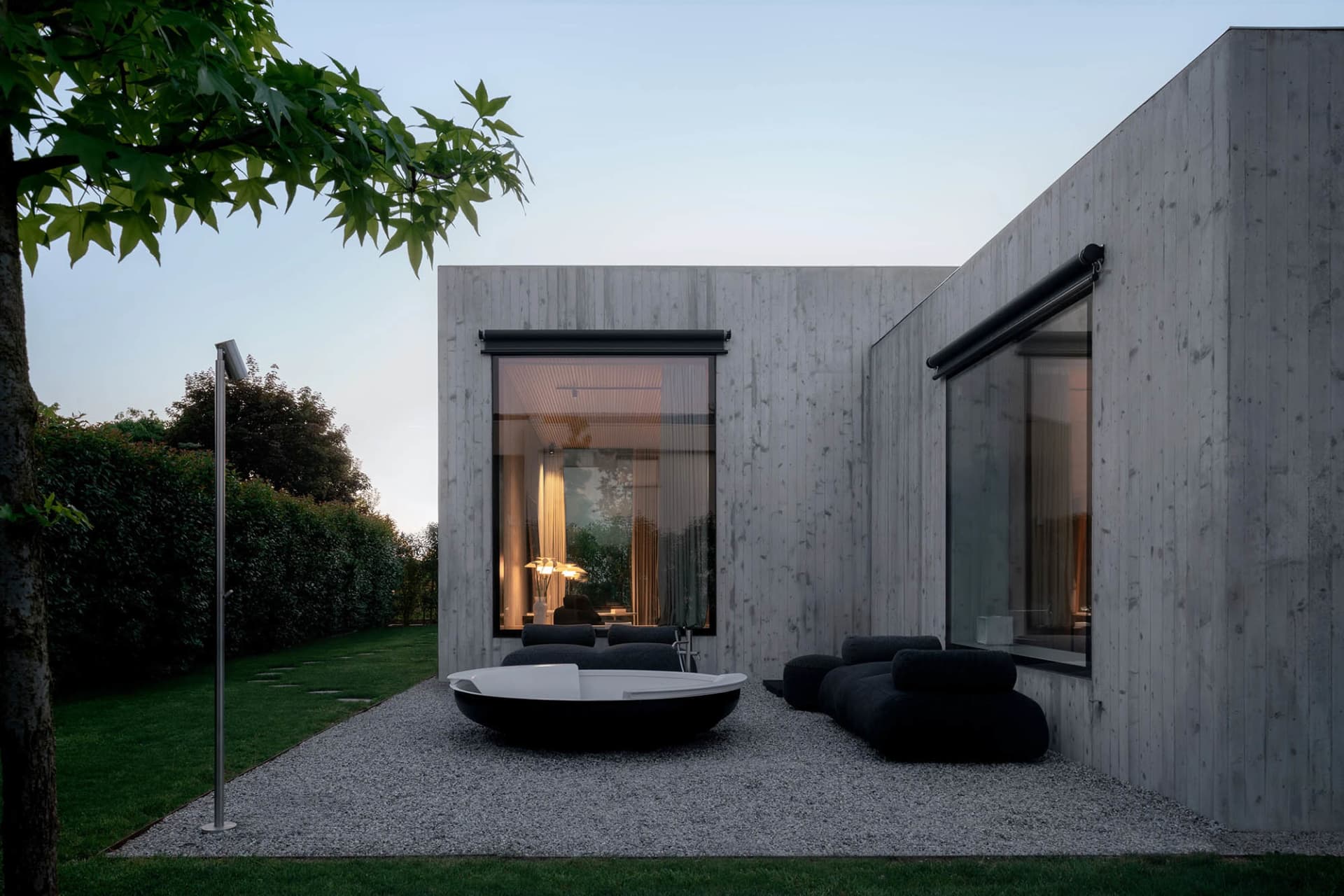 A modern minimalist exterior with concrete walls, large windows, and outdoor seating area.