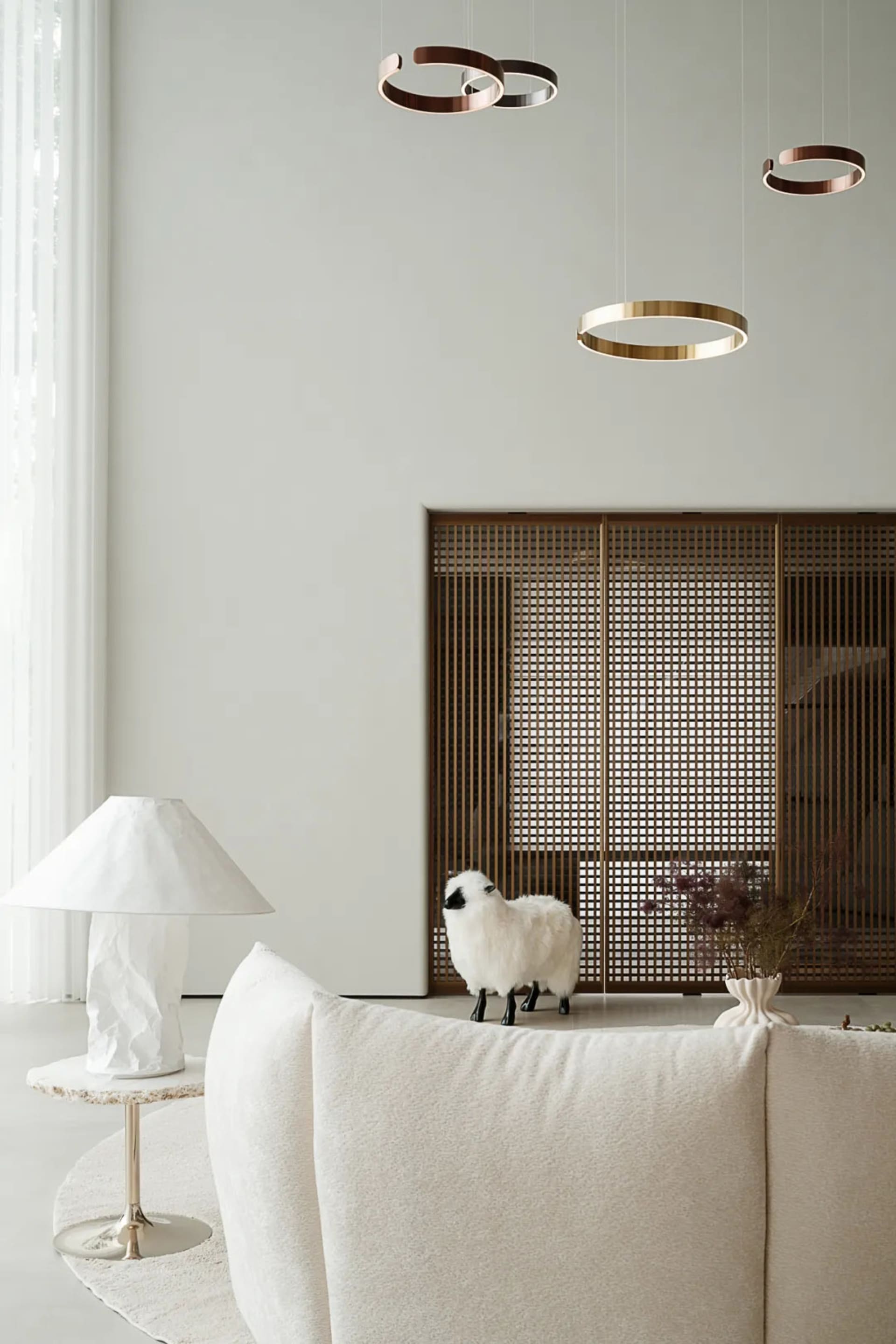 Modern minimalist living room featuring a white sofa, a white table lamp, and a metal decorative wall panel.
