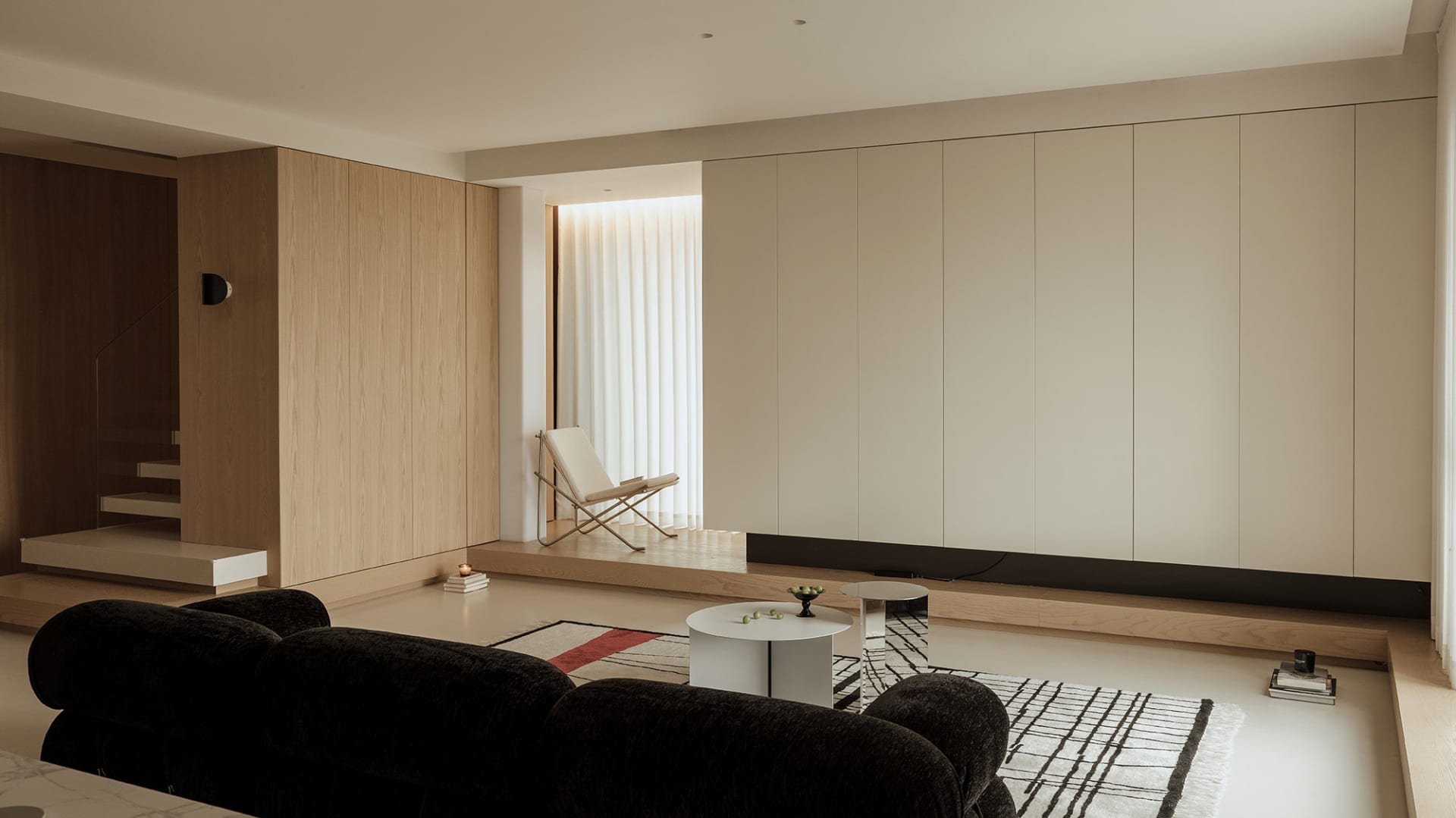 A sleek, minimalist living room with wooden walls, a black sofa, and a white coffee table.
