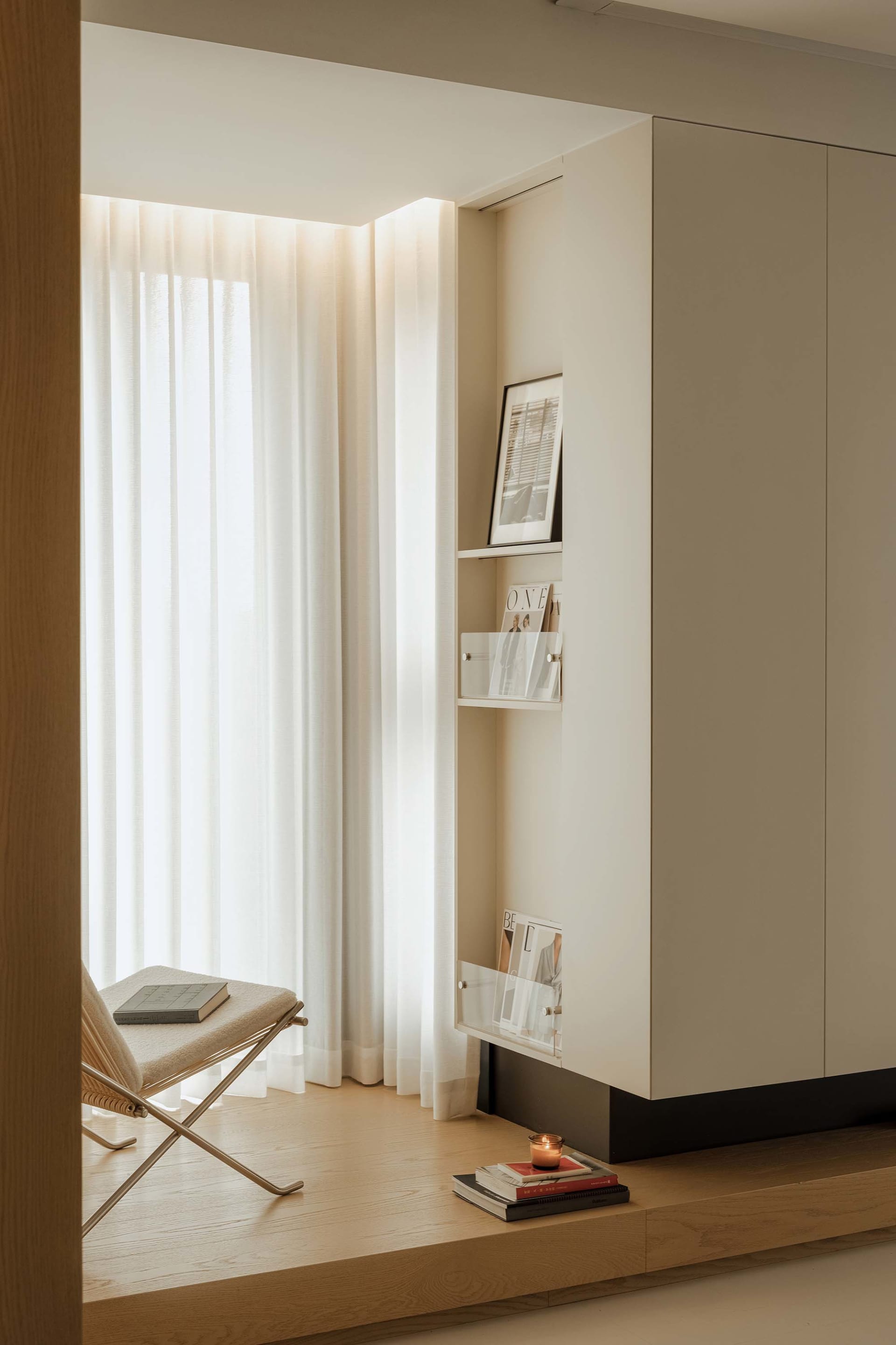 A minimalist residential interior featuring a white fabric chair, wooden surfaces, and metal accents.