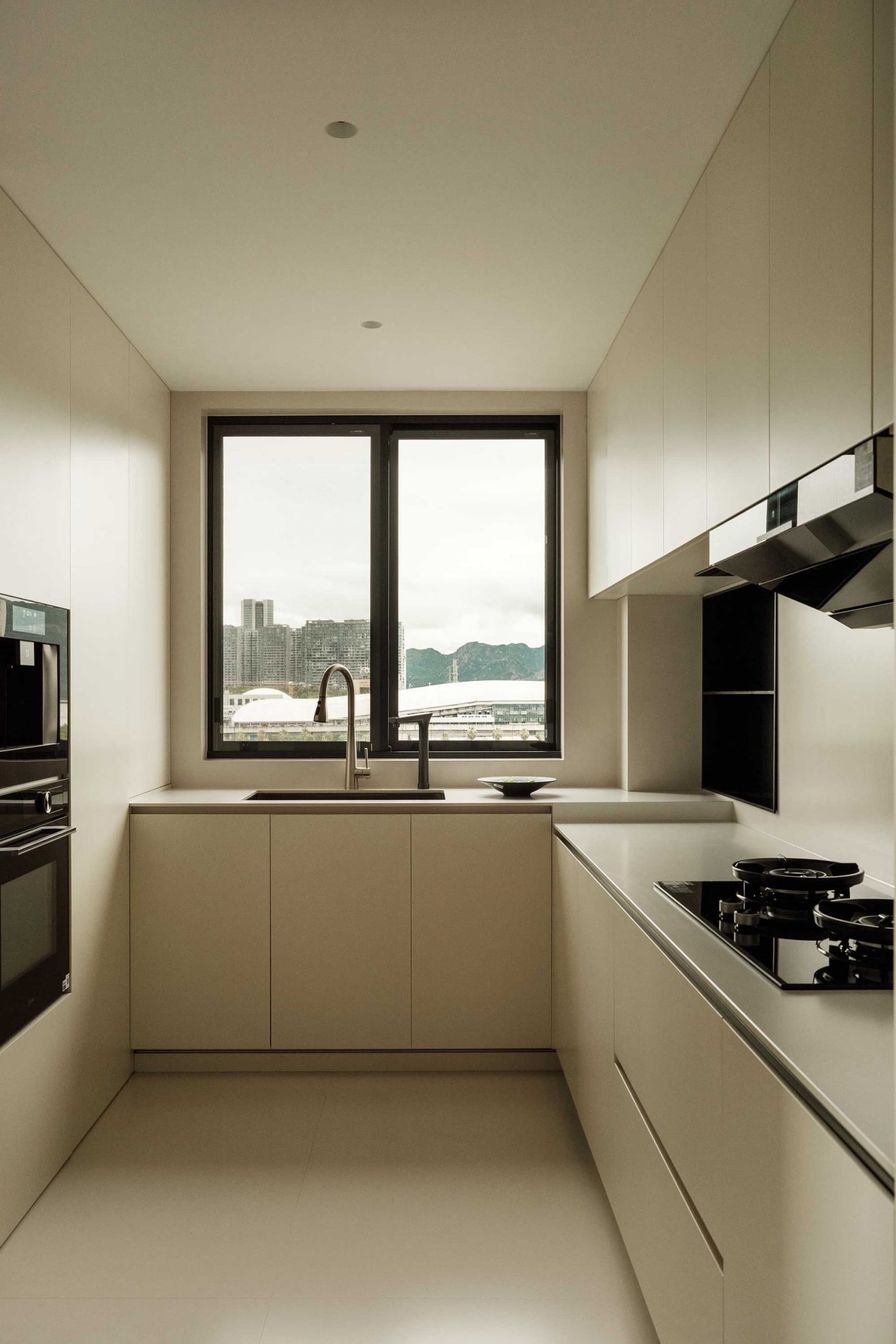 一間現代簡約的白色廚房,設有大型窗戶,可眺望城市景觀與綠意山景。