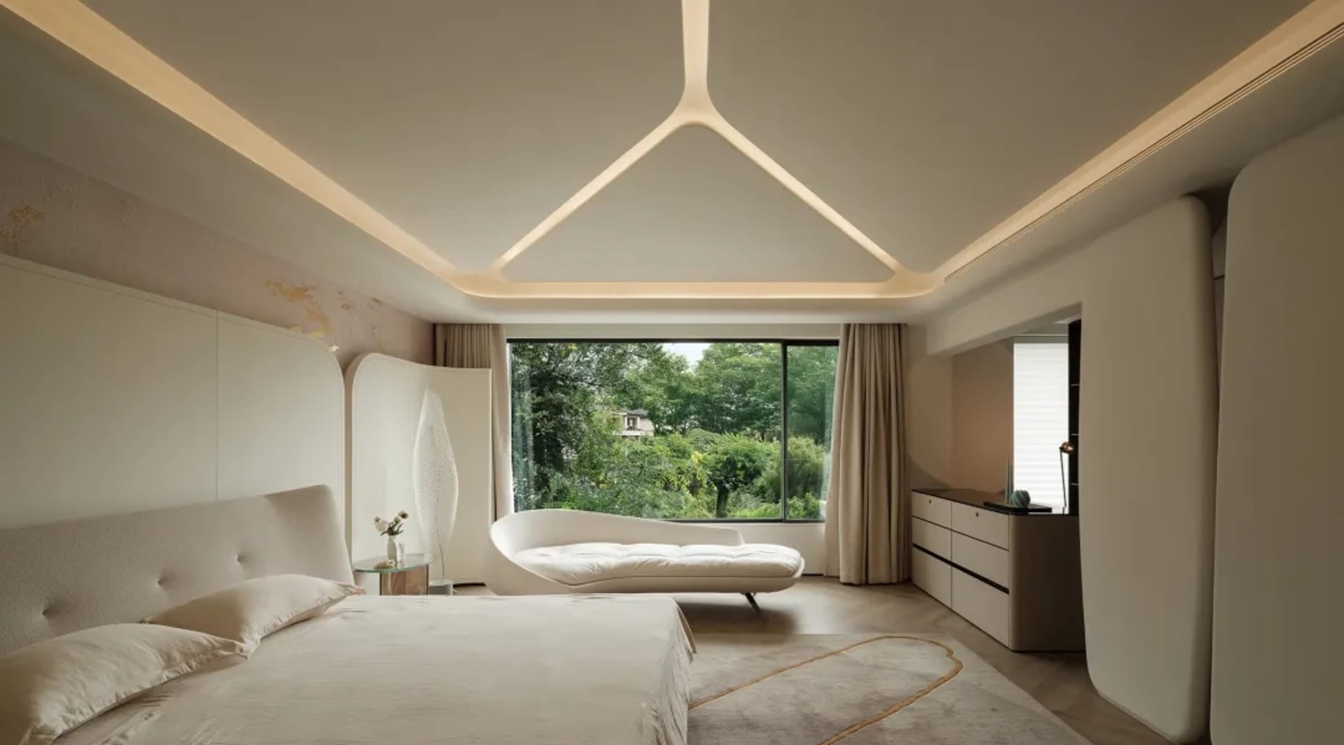A modern bedroom with neutral colors, including a bed with a curved headboard, a white lounge chair, and a large window with 