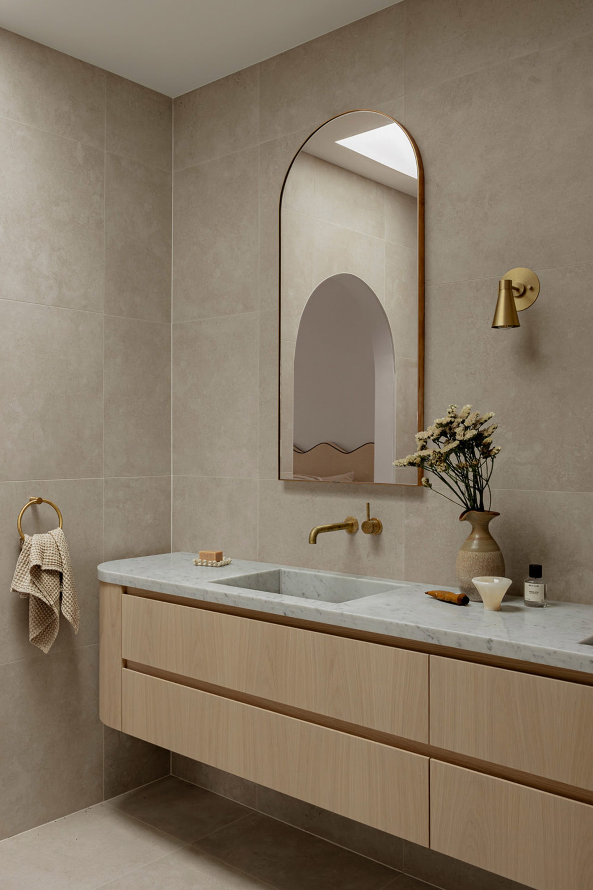 Modern bathroom featuring a marble countertop, concrete sink, oak vanity, brass fixtures, and a minimalist design.