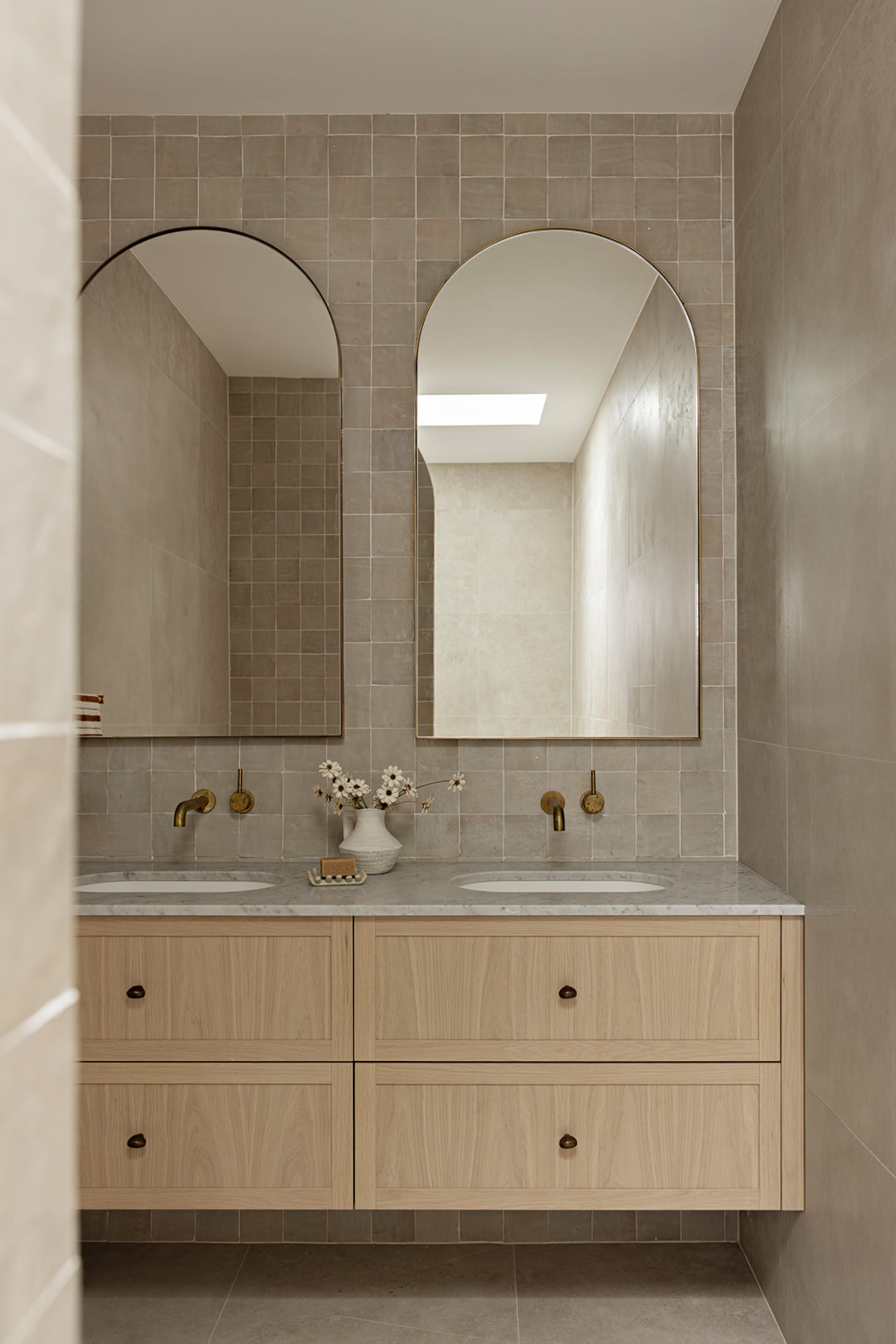 A modern bathroom featuring double sinks, tiled walls, marble countertop, and wooden vanity.