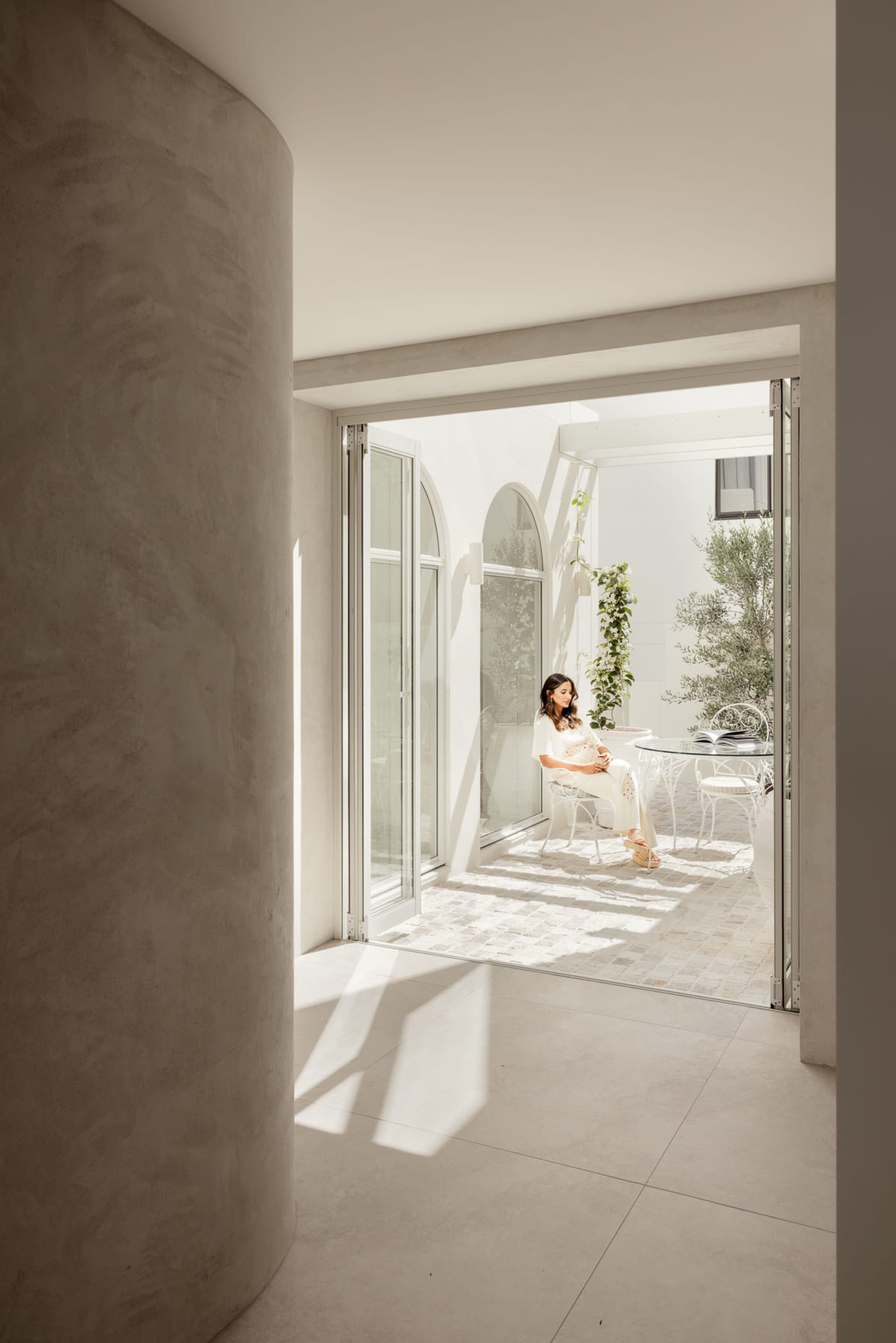 A modern interior with light concrete walls and a woman sitting on a chair in a bright, spacious room.