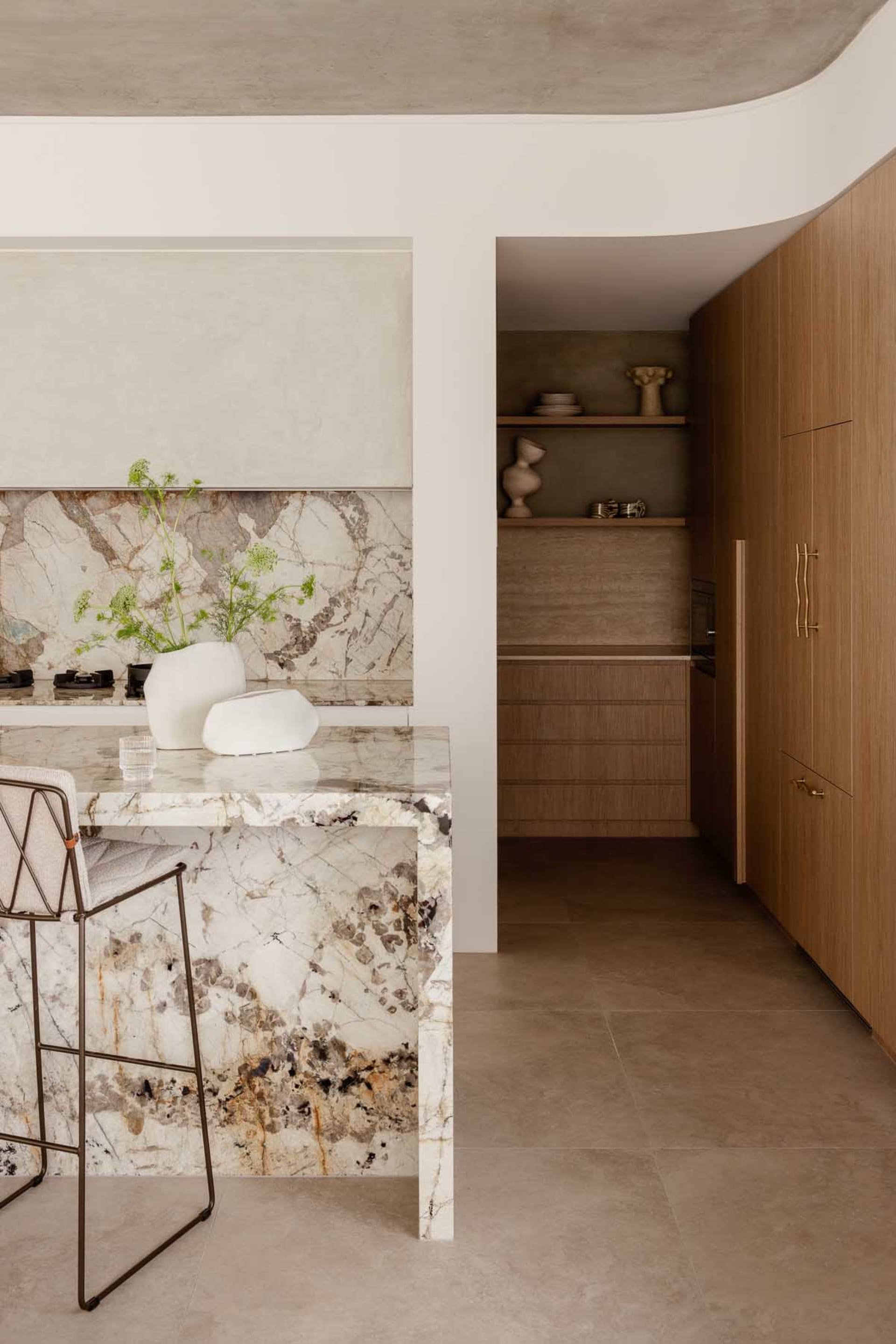 Marble kitchen counter with a white vase containing green plants and a glass of water on it.