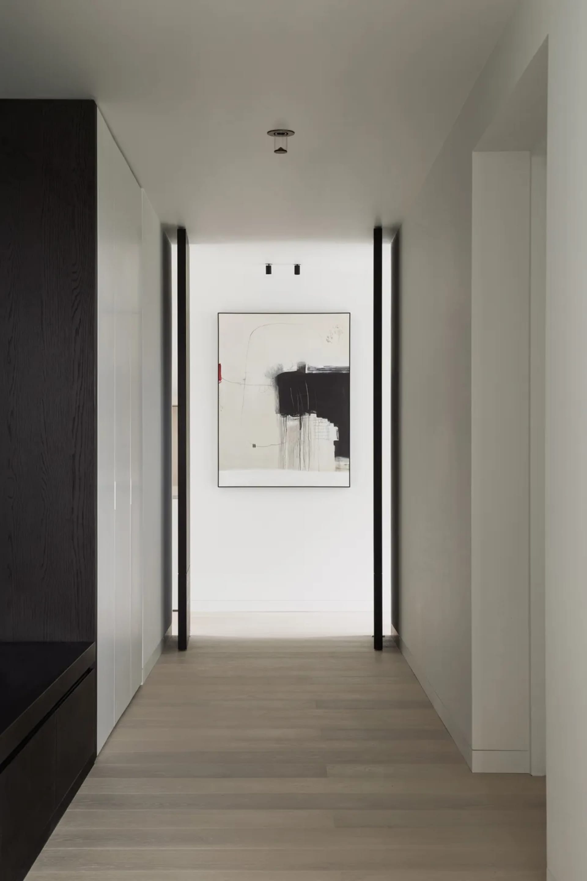 A modern hallway with minimalist black and white decor, featuring abstract art on the wall and dark wooden cabinets.