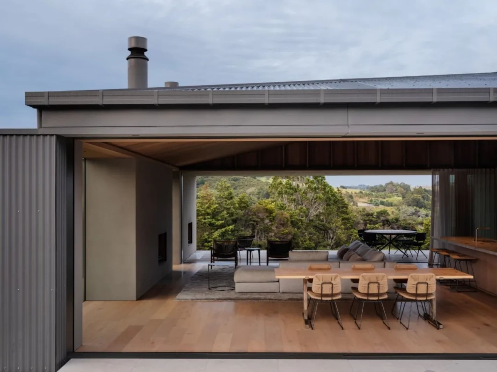 Modern residential interior with wood floors, concrete walls, and glass windows overlooking a natural landscape.