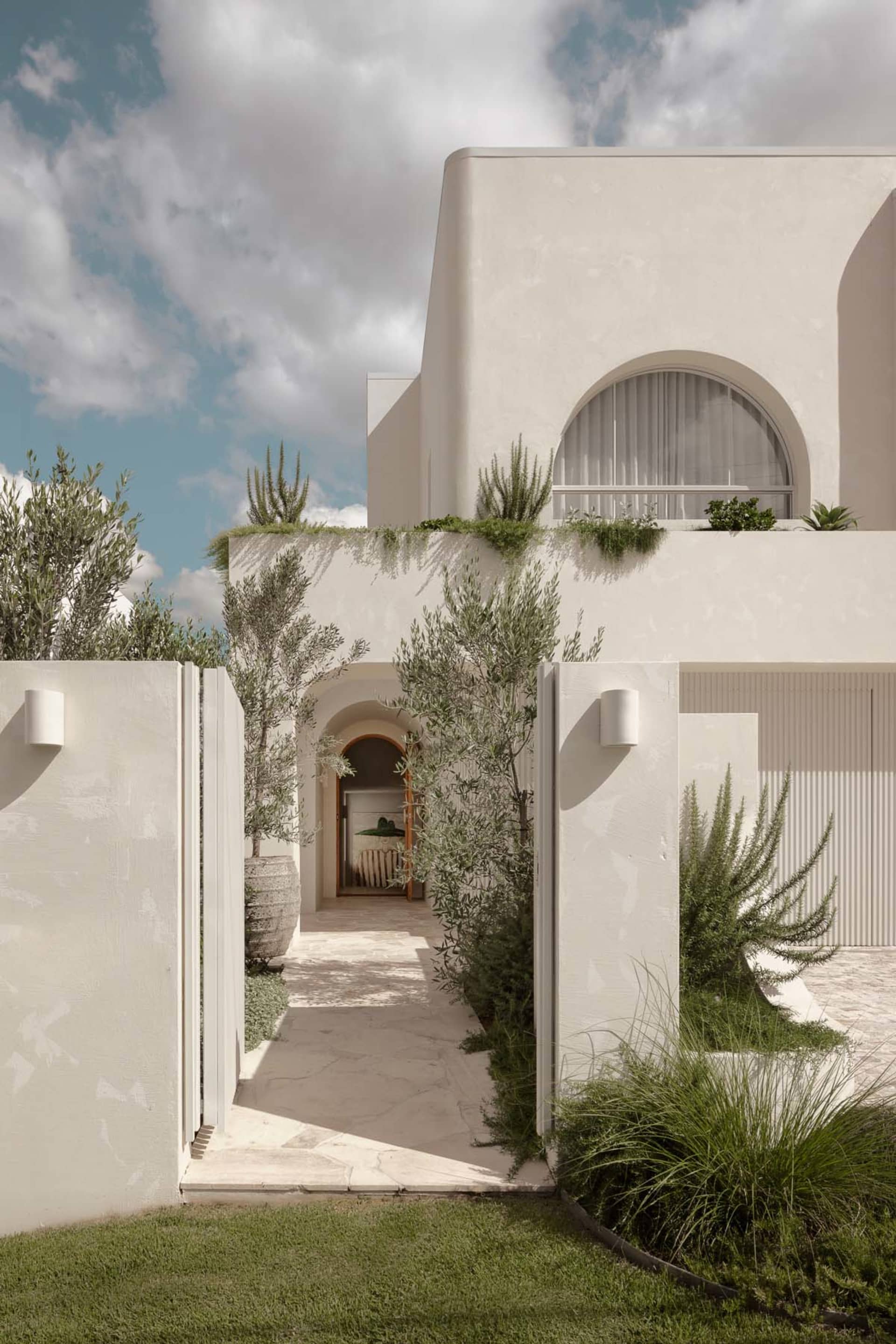 Modern home with white rendered stone exterior, featuring large windows and lush greenery.