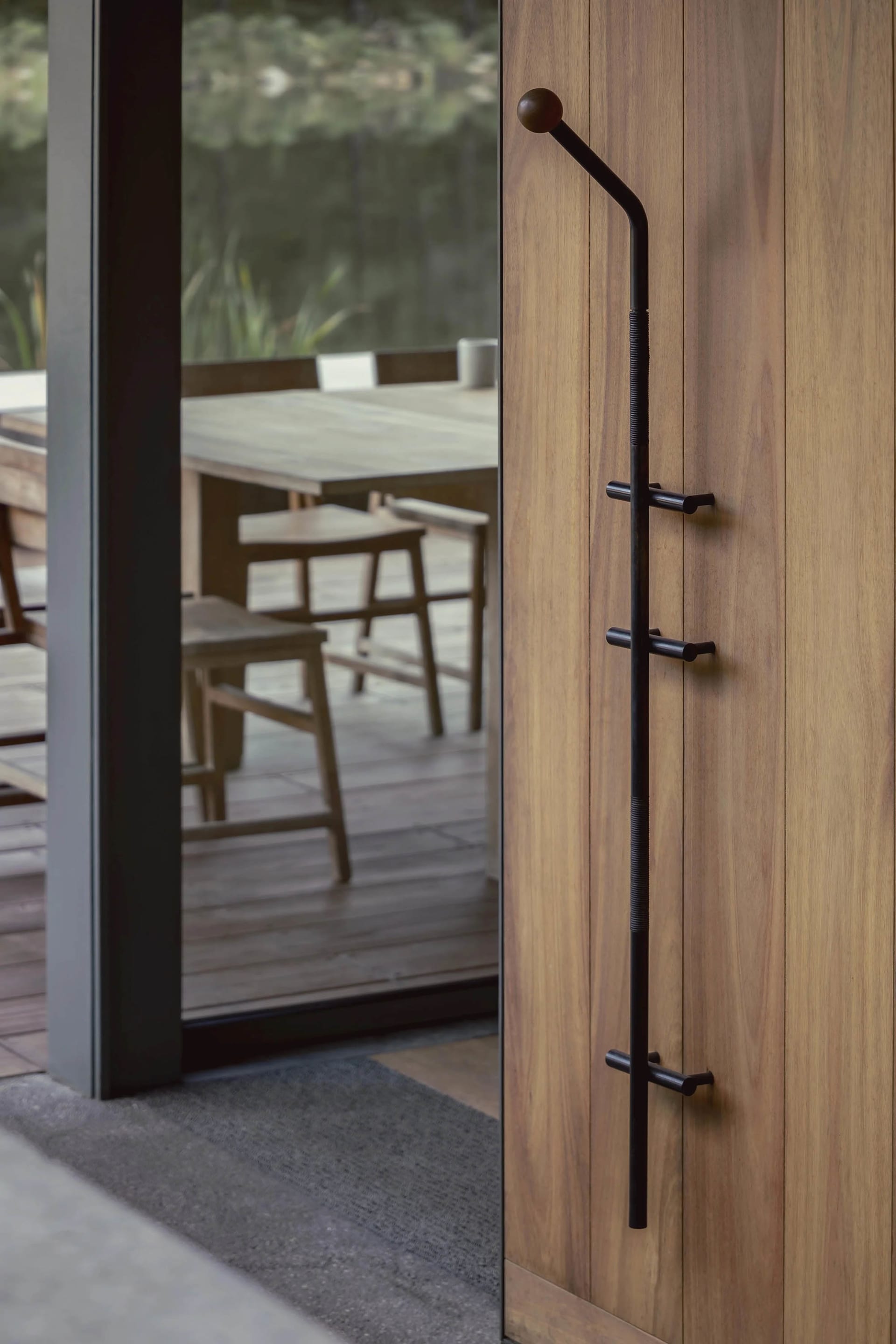A modern wooden door with a black metal handle and hook on a wooden floor.