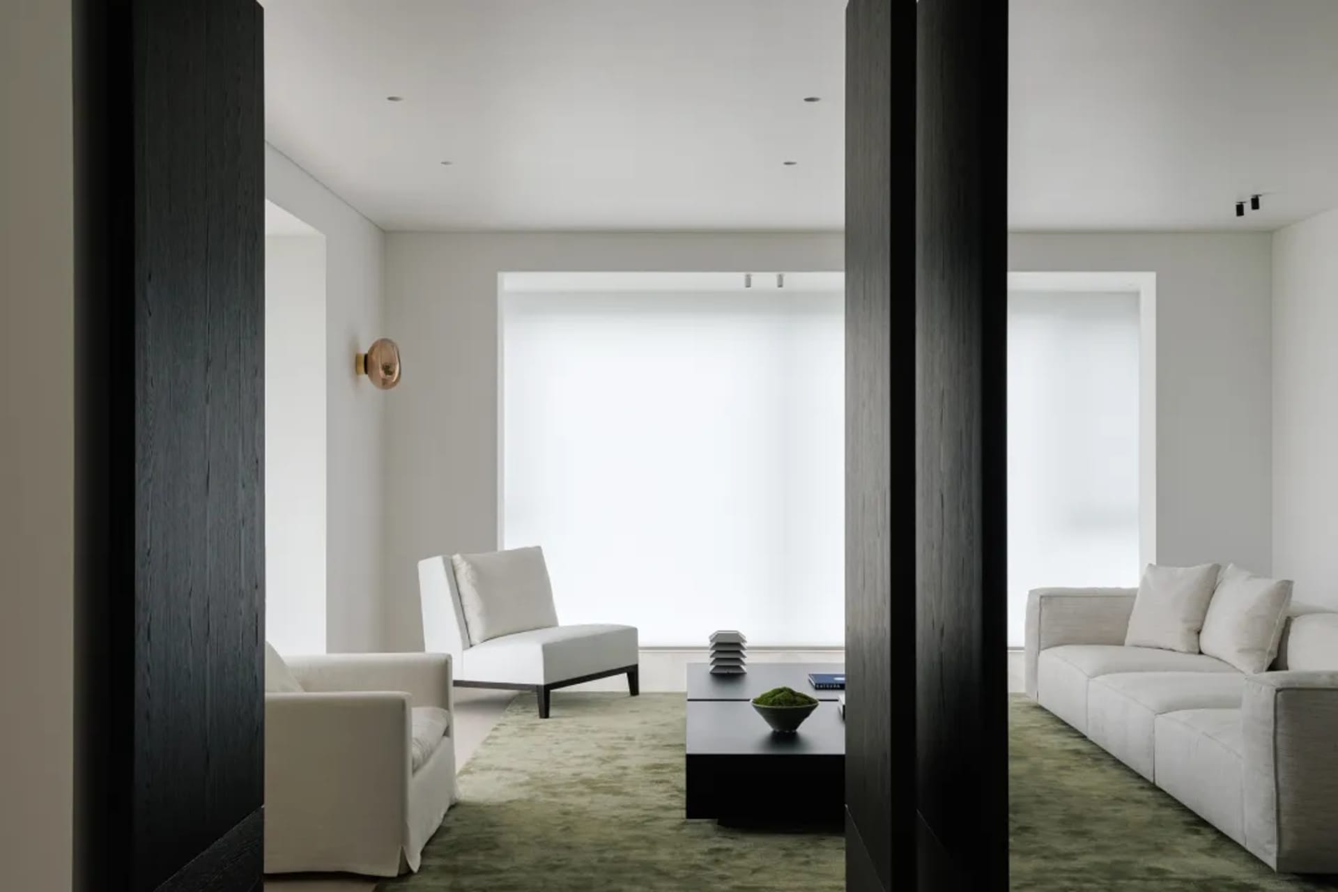 A minimalist living room featuring a sofa and armchairs, with a green rug and a dark coffee table.