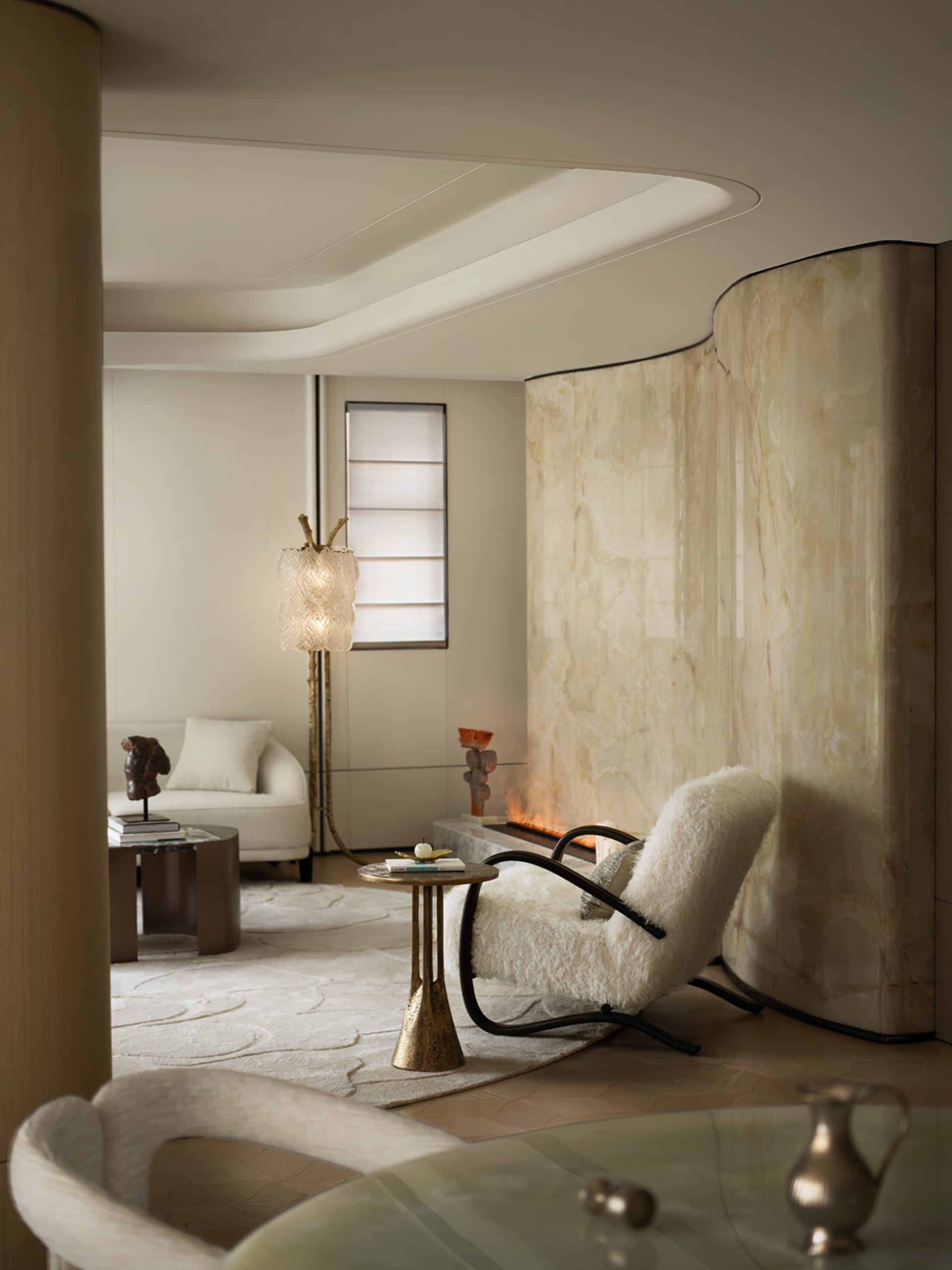 A modern living room with white marble walls and floor, featuring a circular white sofa with colorful cushions and large wind
