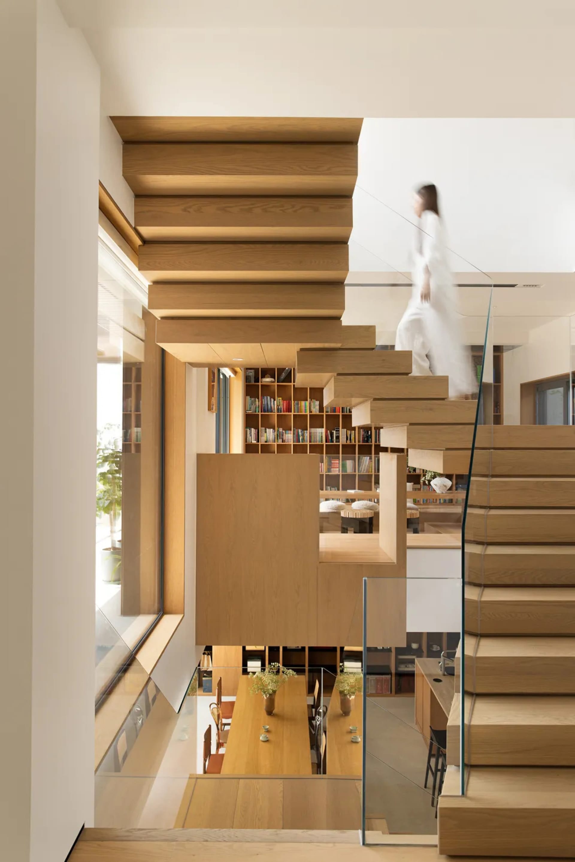 A modern residential library featuring wooden shelving and a glass staircase.