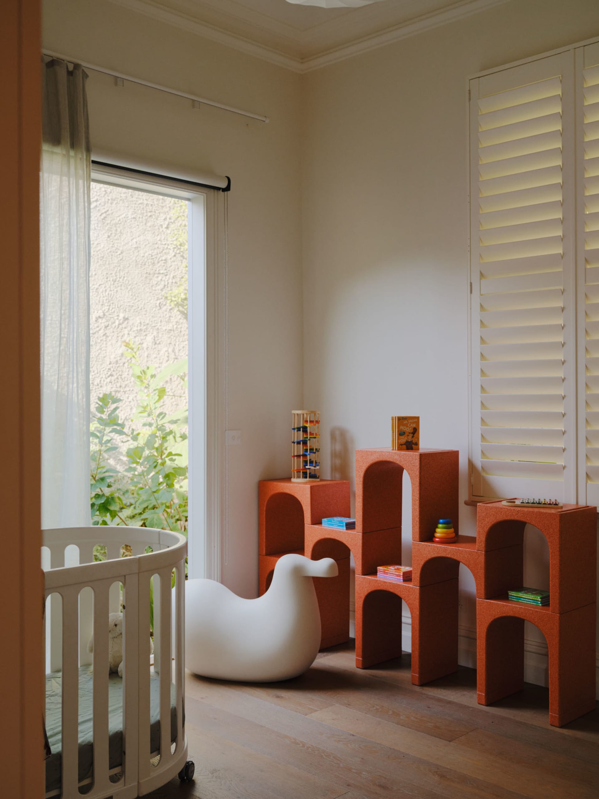 A modern children's bedroom featuring white furniture with bird-shaped armé and orange modular shelving units with children's
