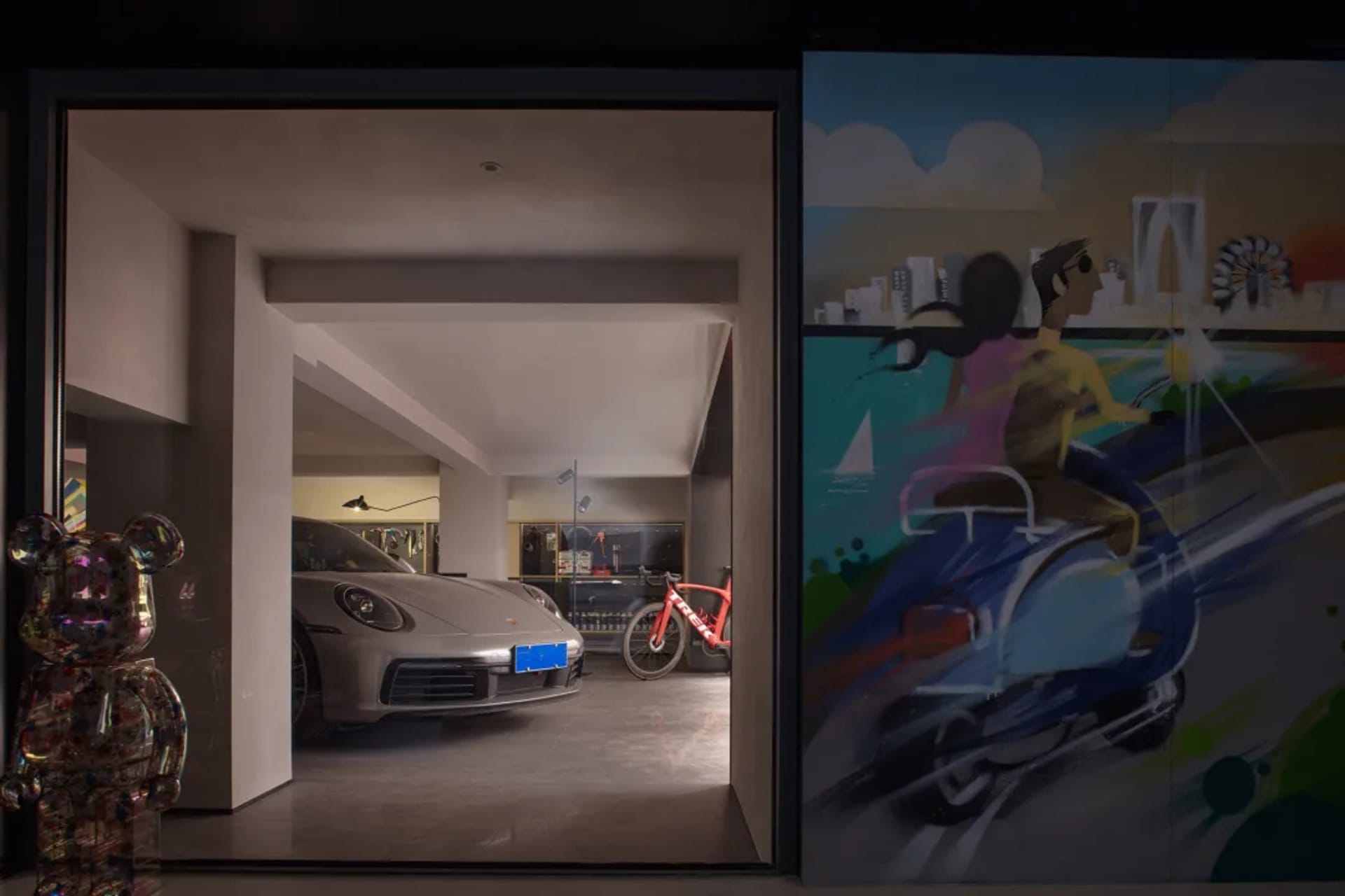 A modern garage featuring metallic elements and art installations, including a sports car and a painting of two people riding