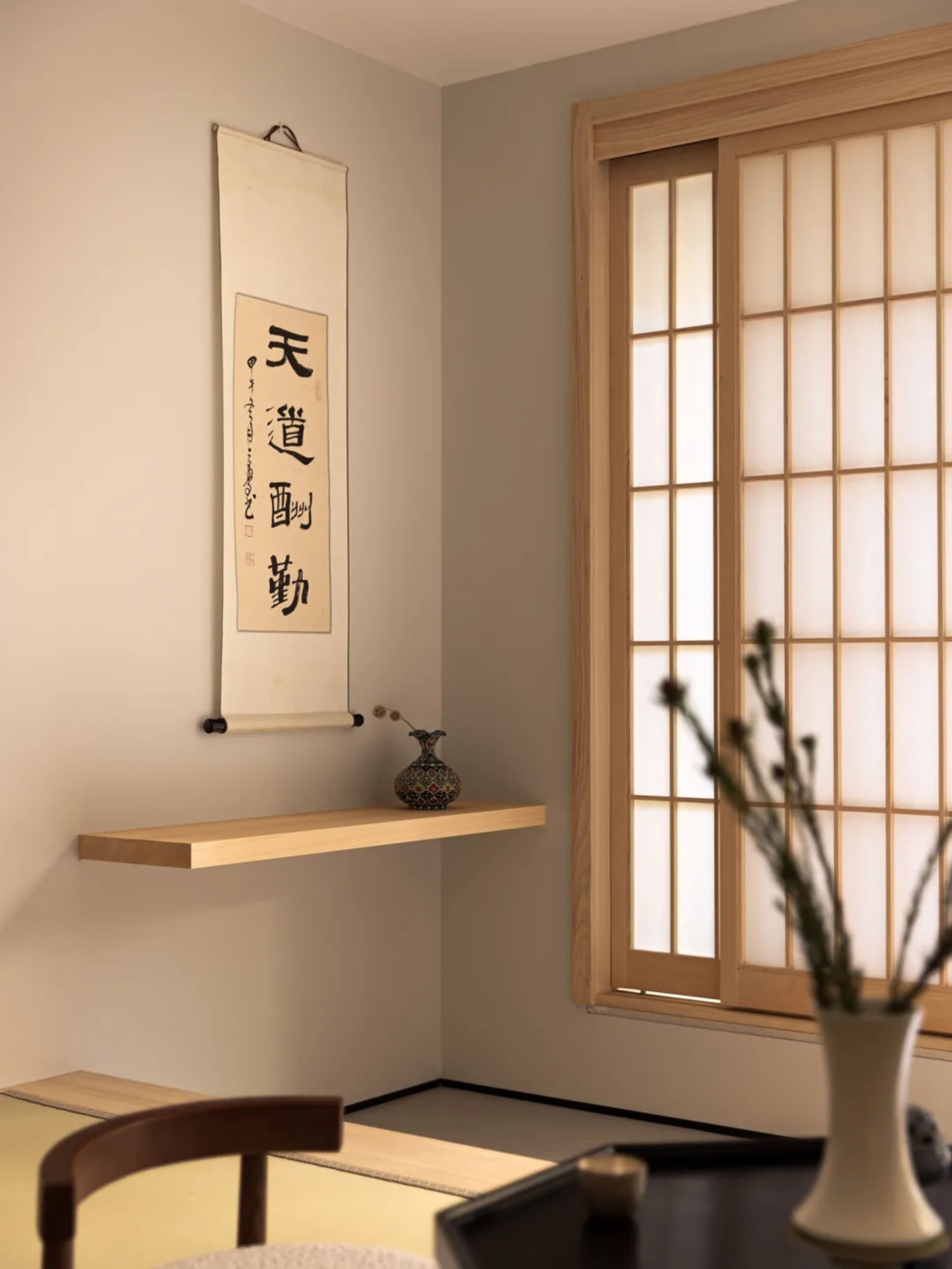 A photograph of a modern minimalist interior space featuring a wooden floating shelf, a traditional sliding door, and a vase