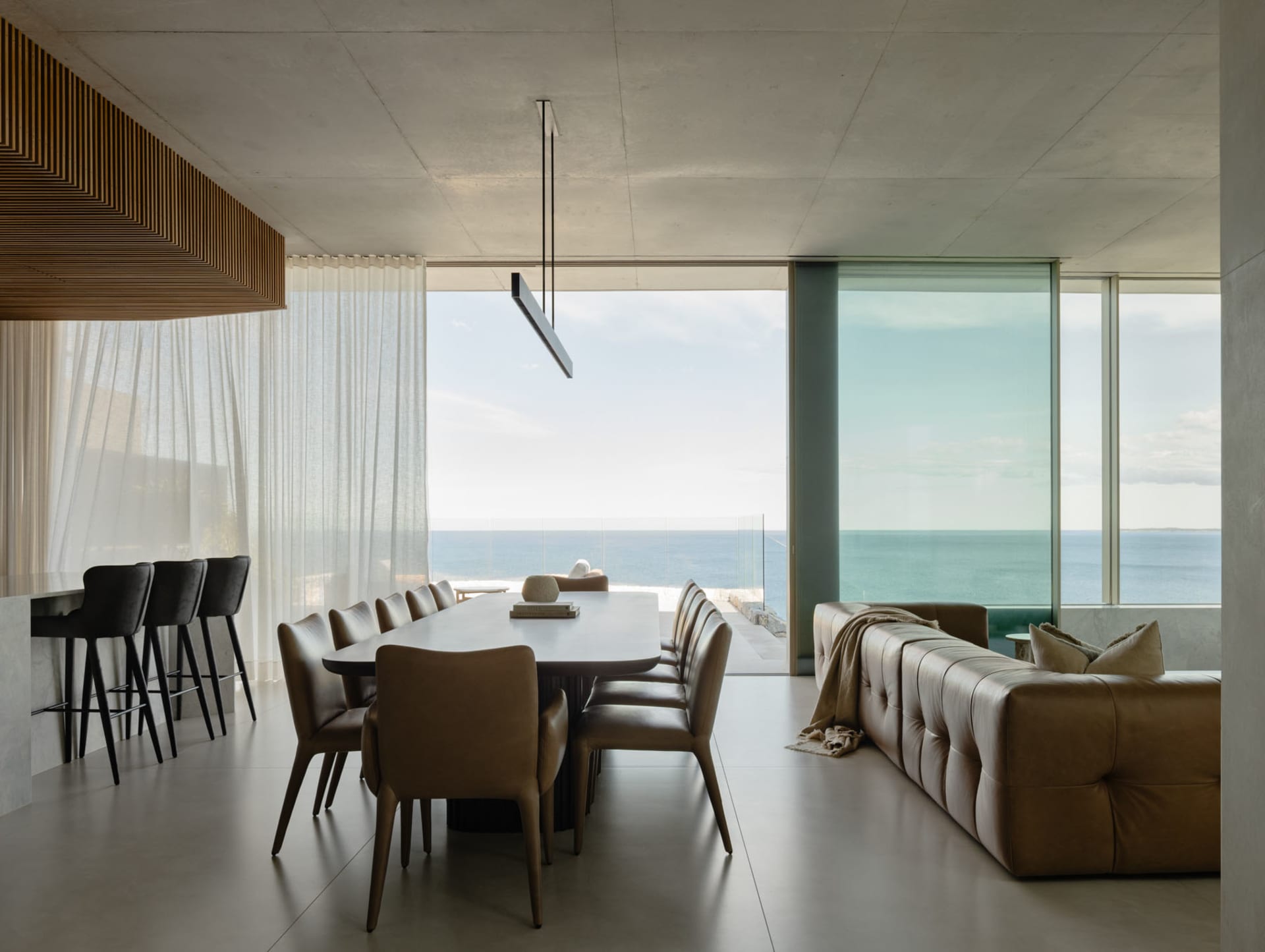 A modern living room with concrete and glass walls, large windows overlooking the ocean, and minimalist furniture.