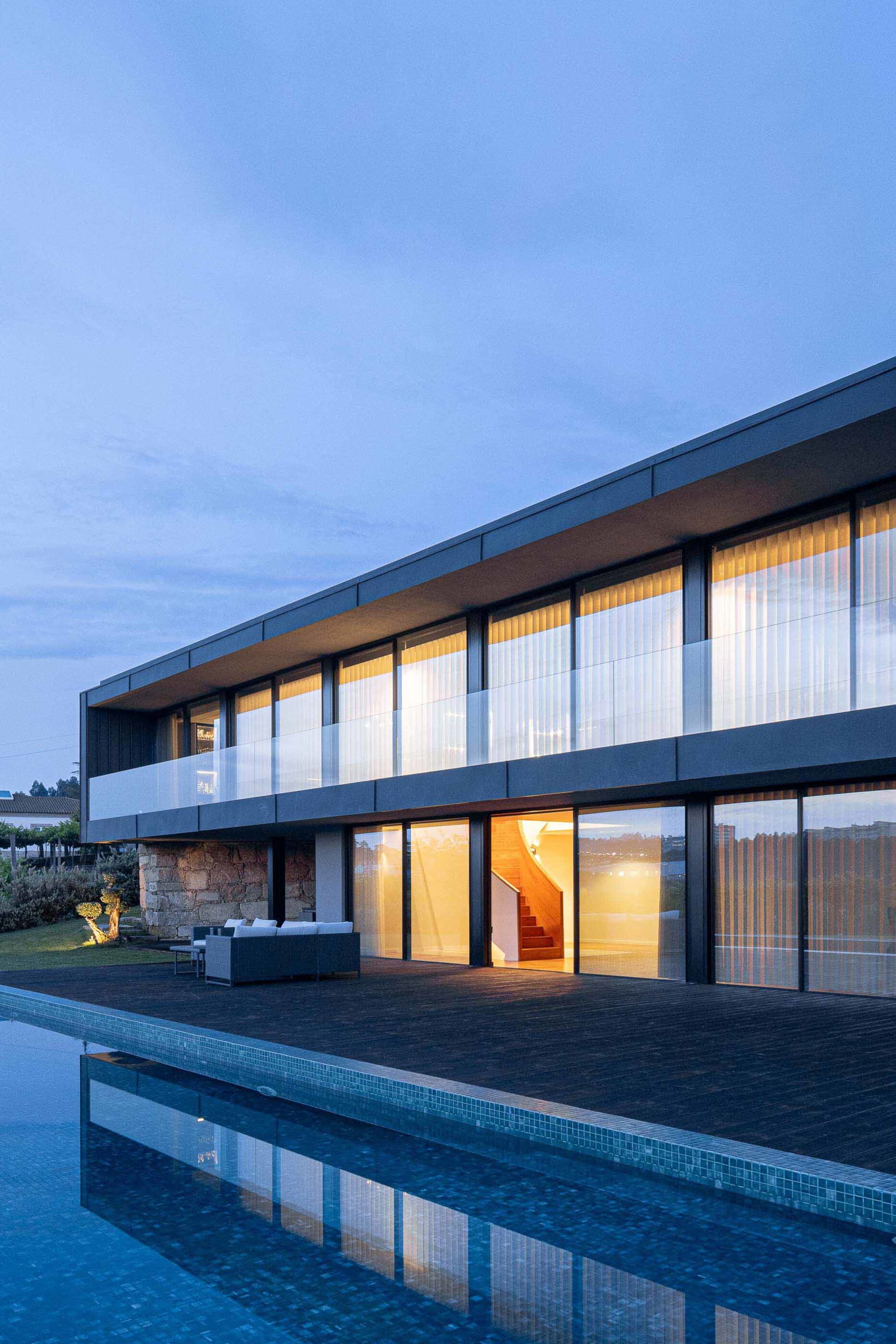 Modern residential house with glass walls and stone accents, featuring a swimming pool.