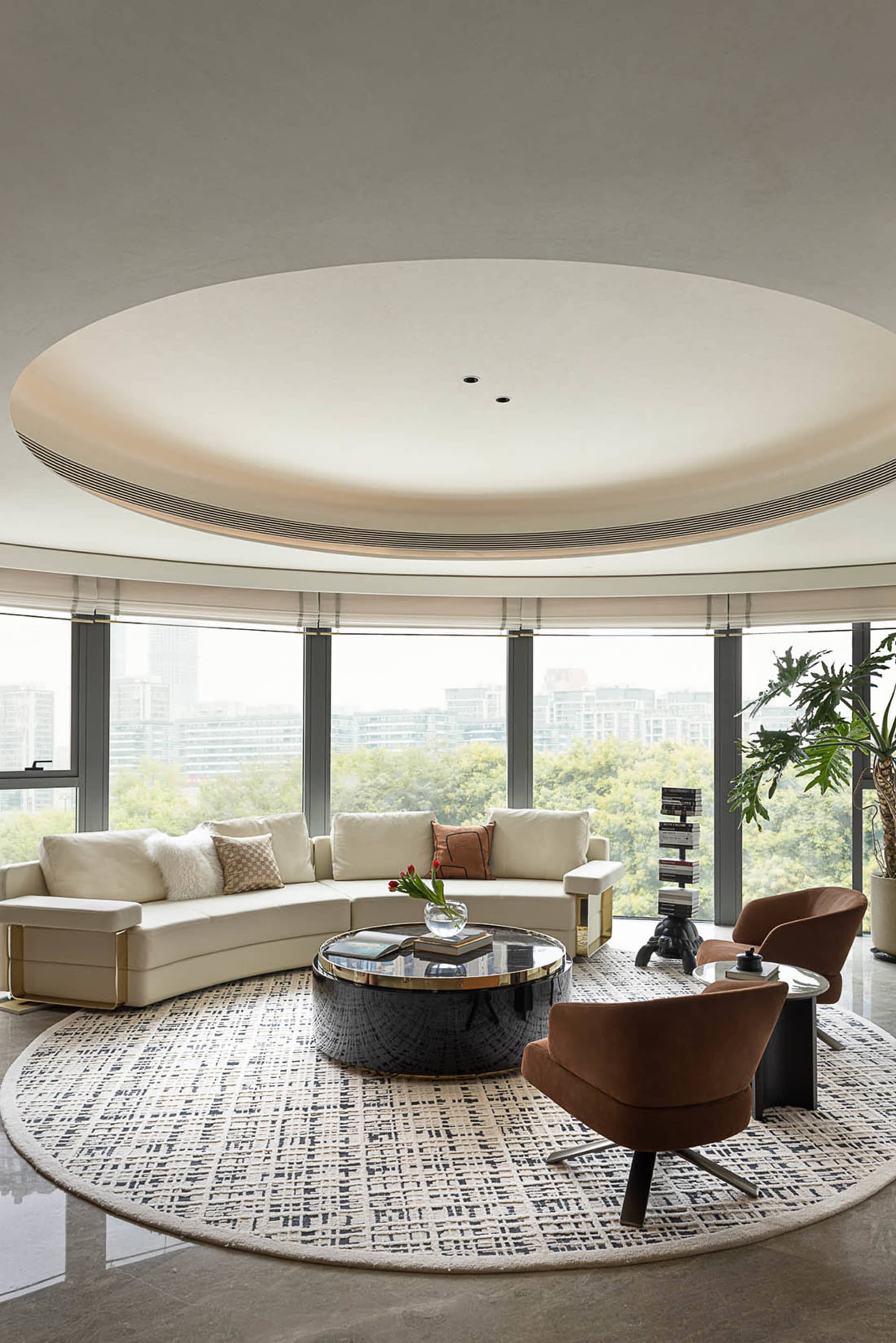 A modern, minimalist living room featuring a white sectional sofa with decorative pillows, a round glass coffee table, and br