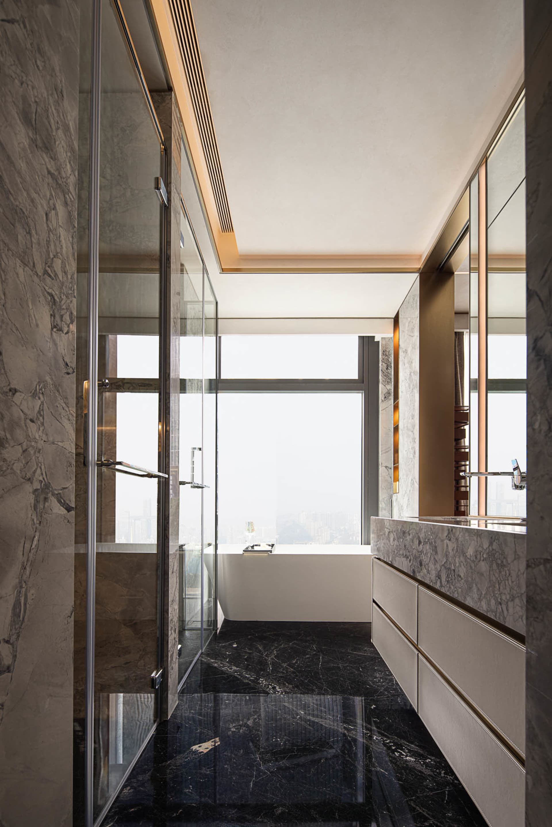 Modern bathroom with marble walls and floor, large windows, and a freestanding bathtub.