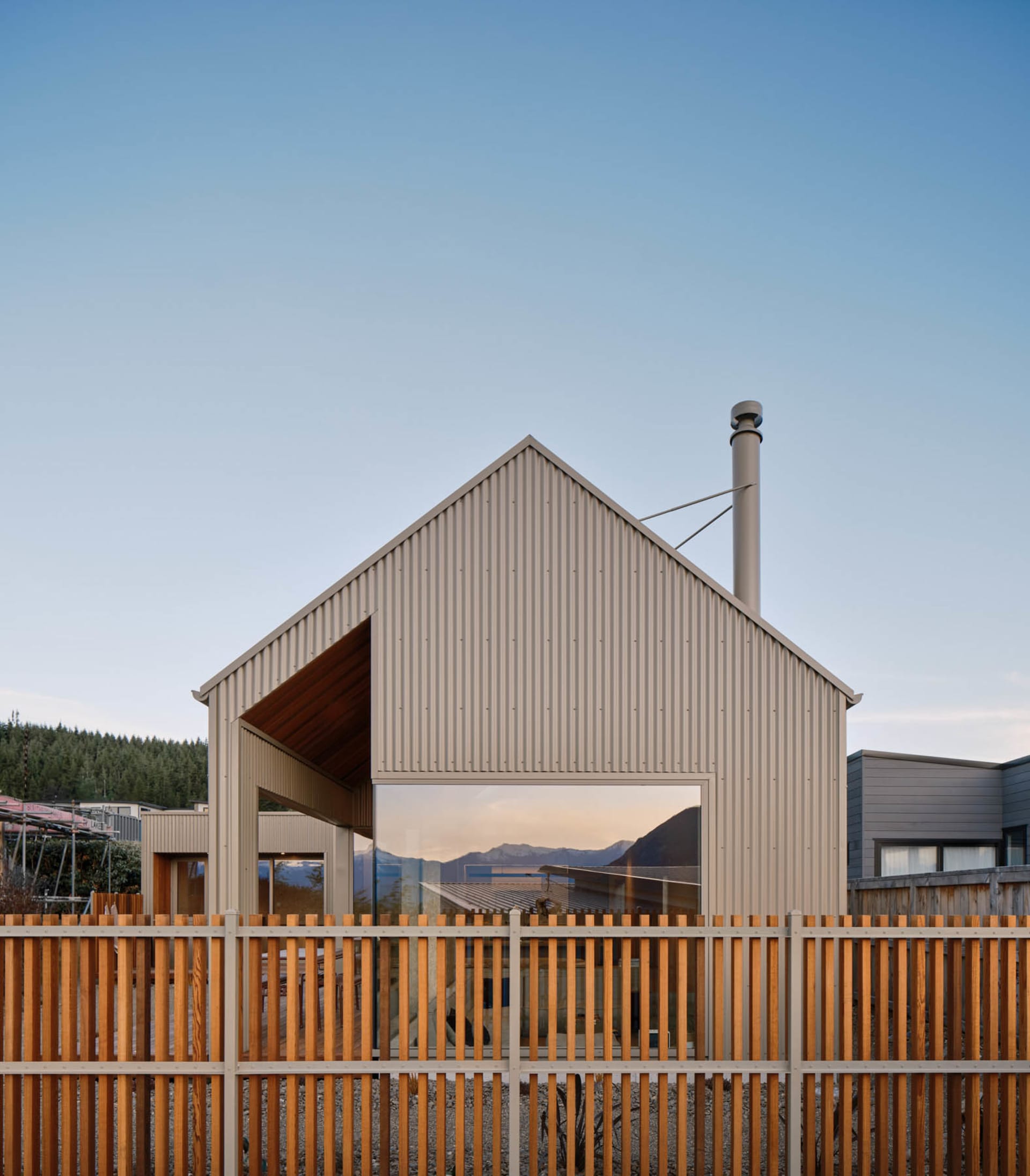 A modern house with a corrugated metal exterior and a large window reflecting the sky and surrounding landscape.