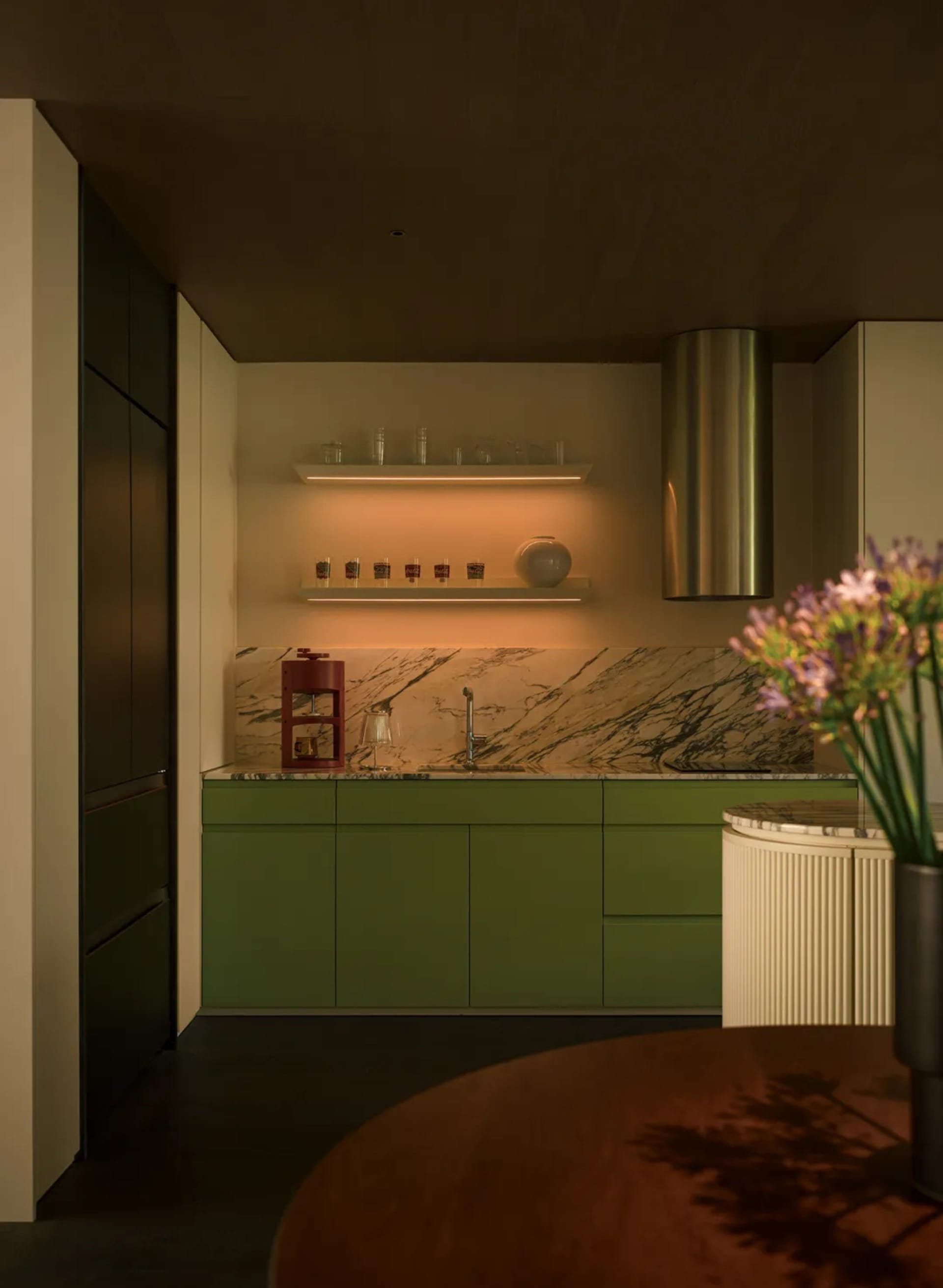A modern kitchen with green cabinets and a marble backsplash.