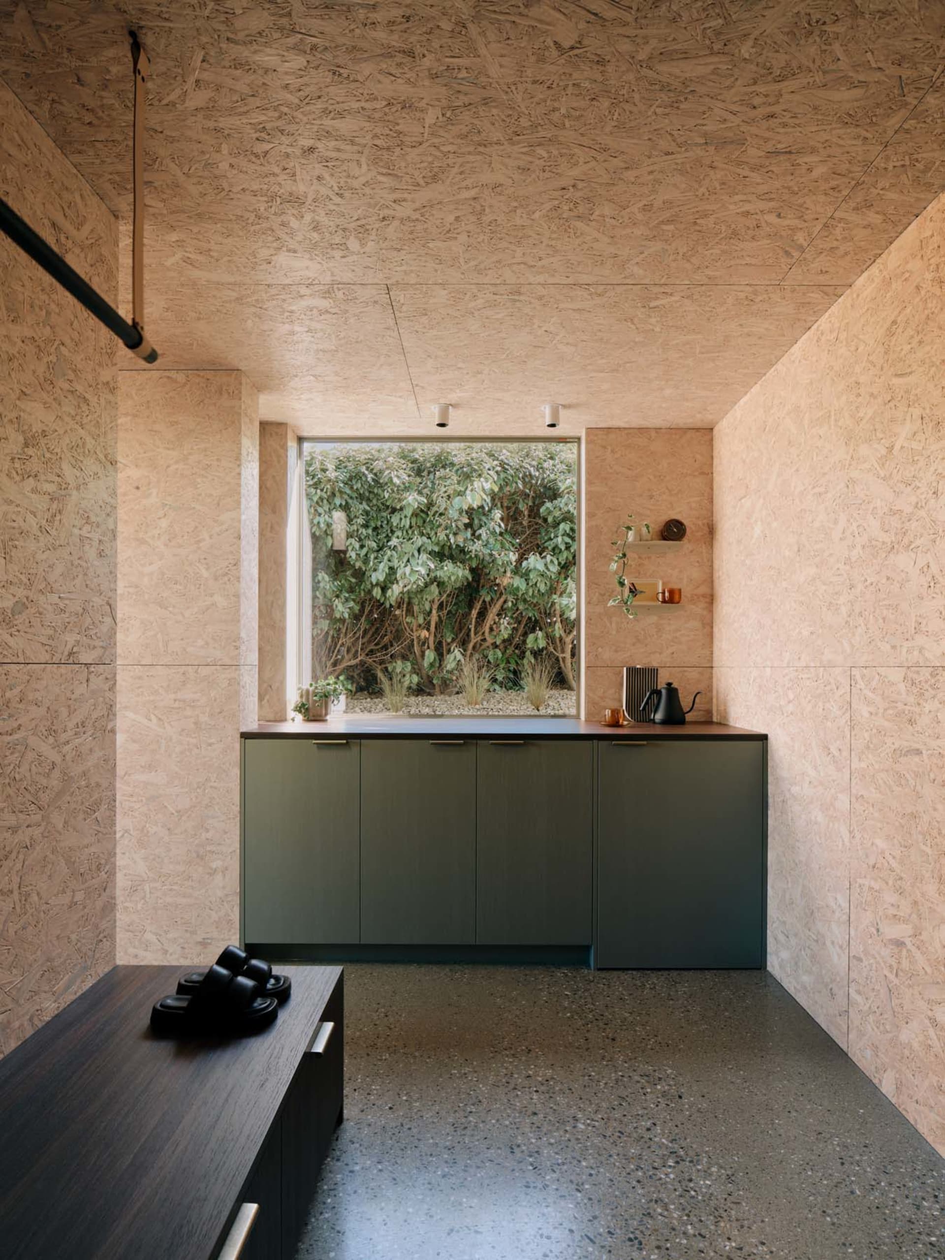 A modern minimalist kitchen with concrete walls and cabinets, featuring a small window with a view of greenery.