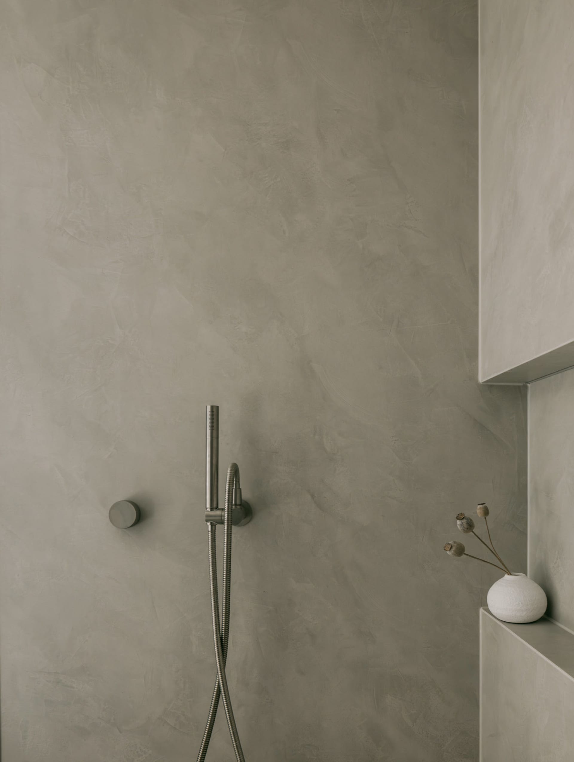 A minimalist bathroom with concrete walls and a hand-held shower head.