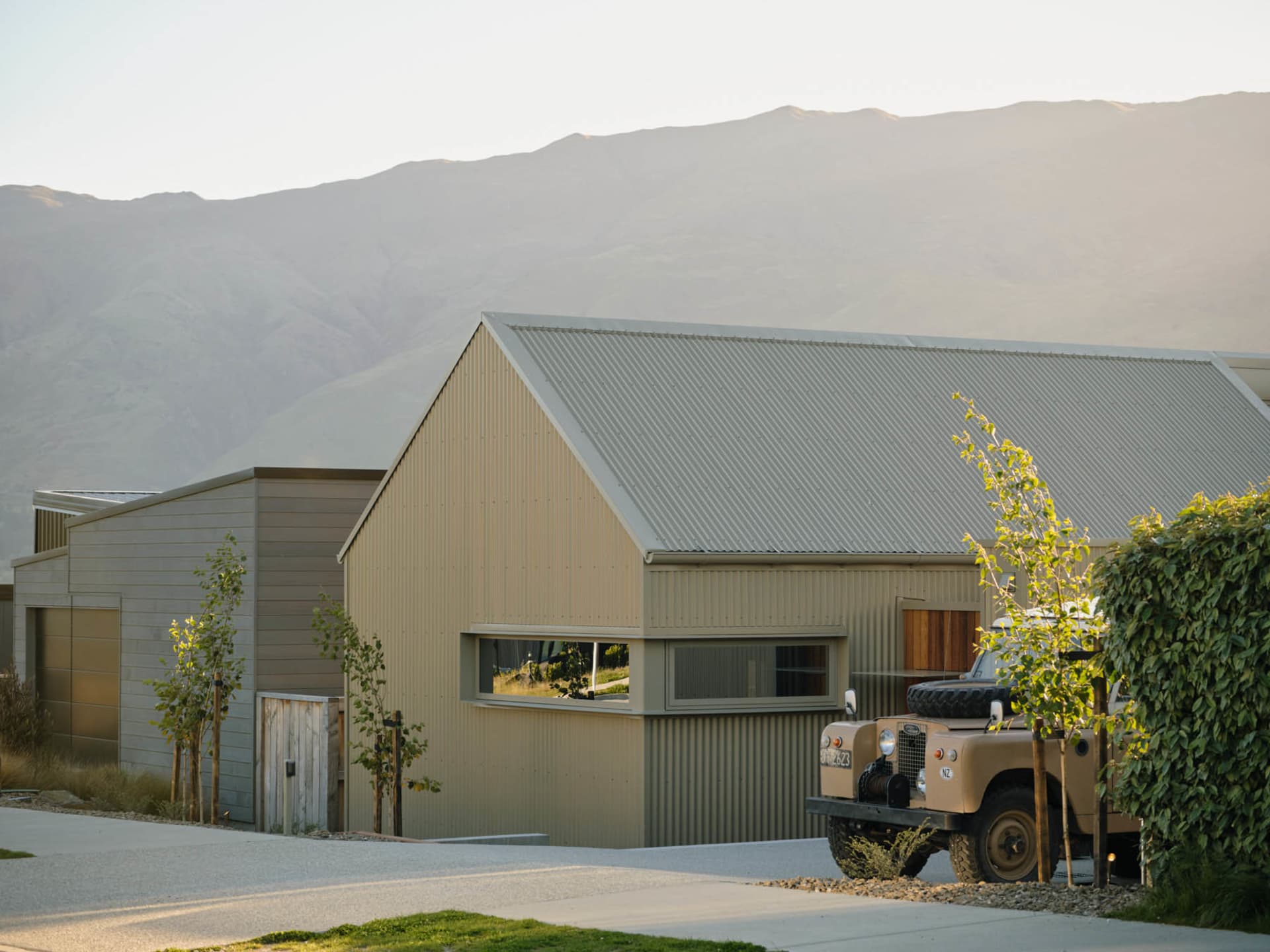 A modern house with a metal siding exterior and a classic off-road vehicle parked nearby. The building sits against a backdro