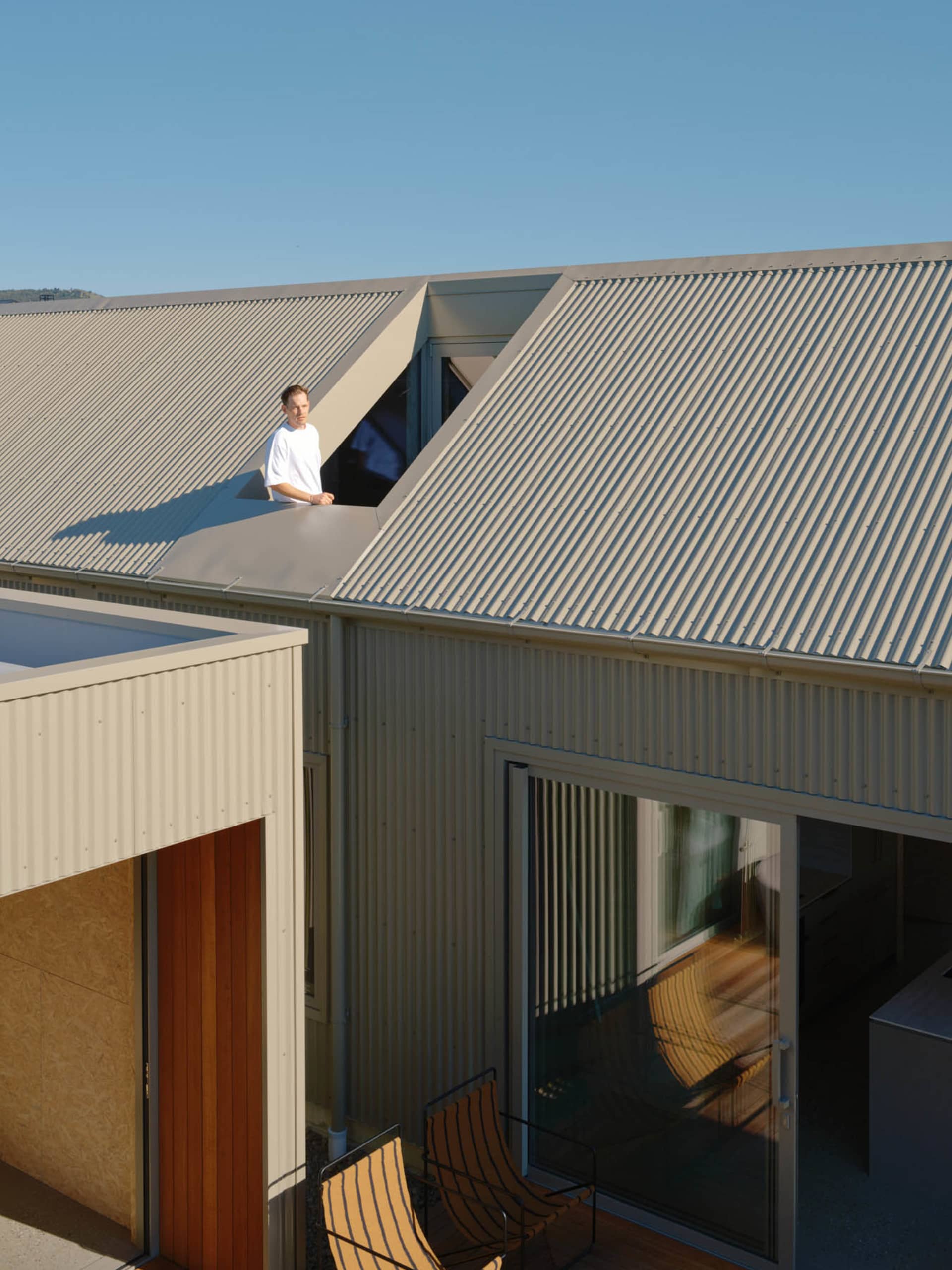 A person standing on the rooftop of a modern house with a corrugated metal roof.