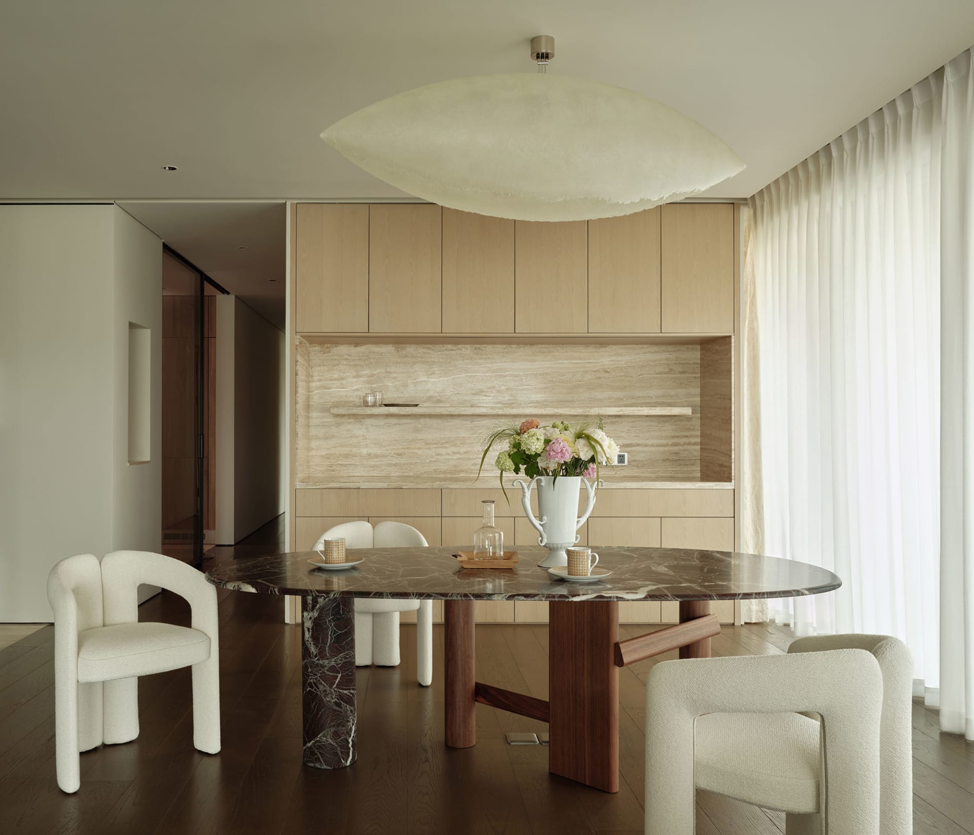 A modern dining room featuring a marble table, wooden chairs, and a fabric accent wall.