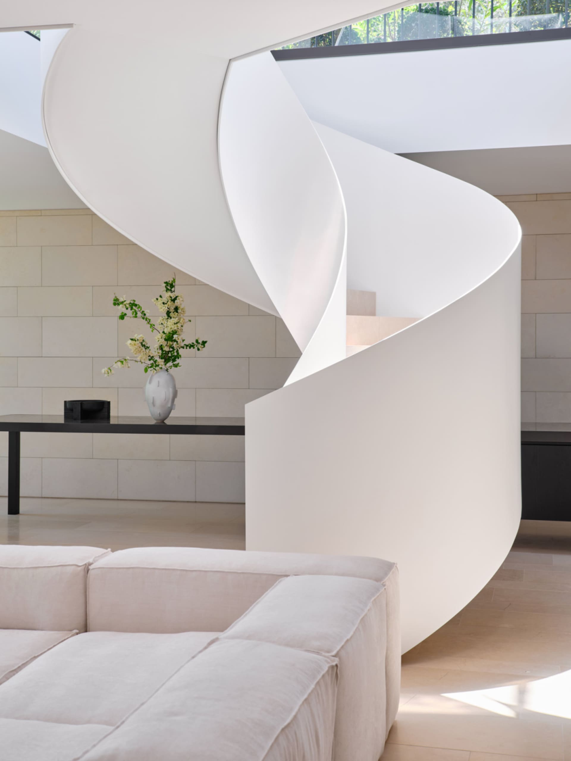 A modern living room with white concrete walls, a spiral staircase, and a white sofa.