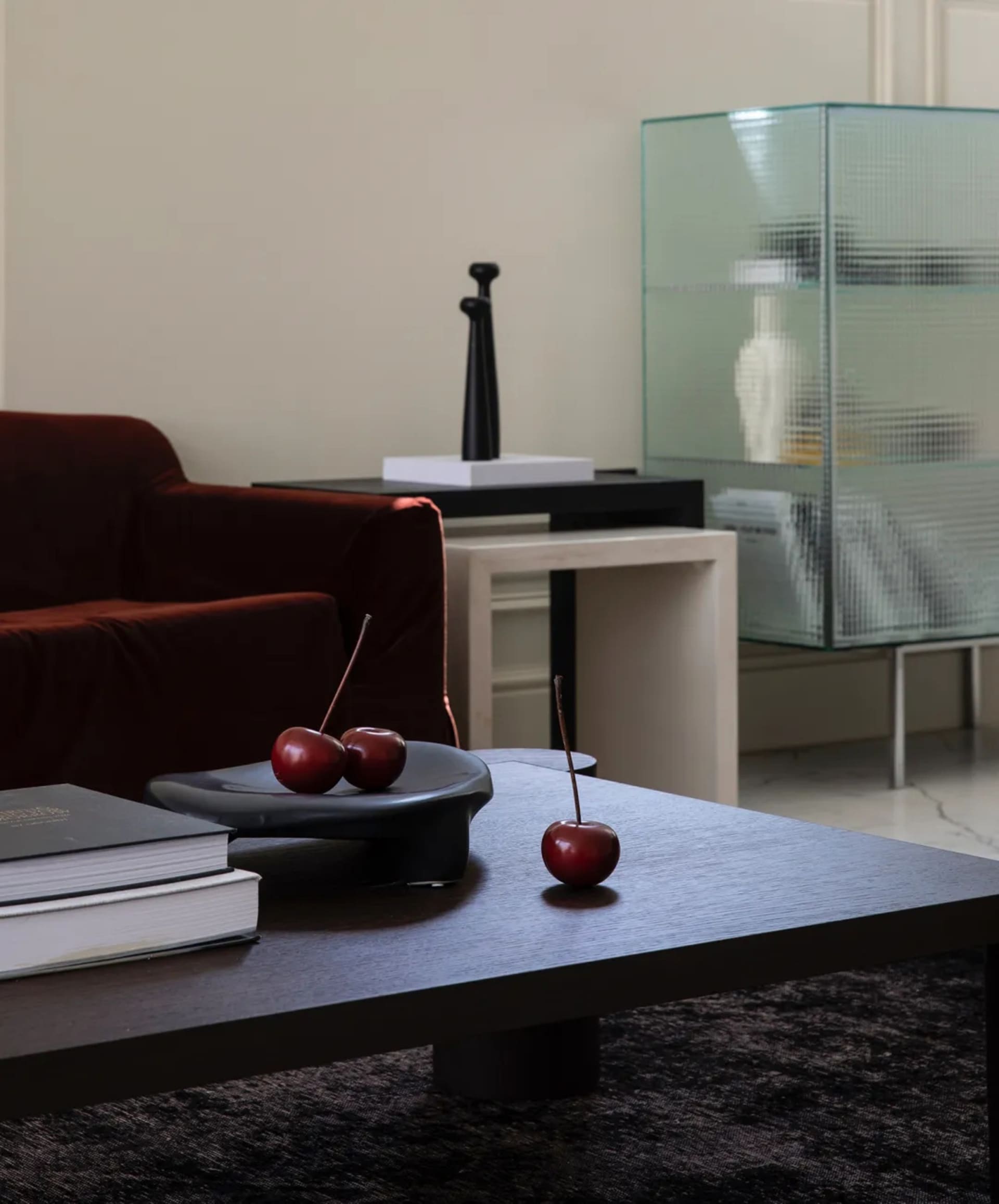 Modern living room with wooden coffee table, red cherries, dark furniture, and glass cabinet.