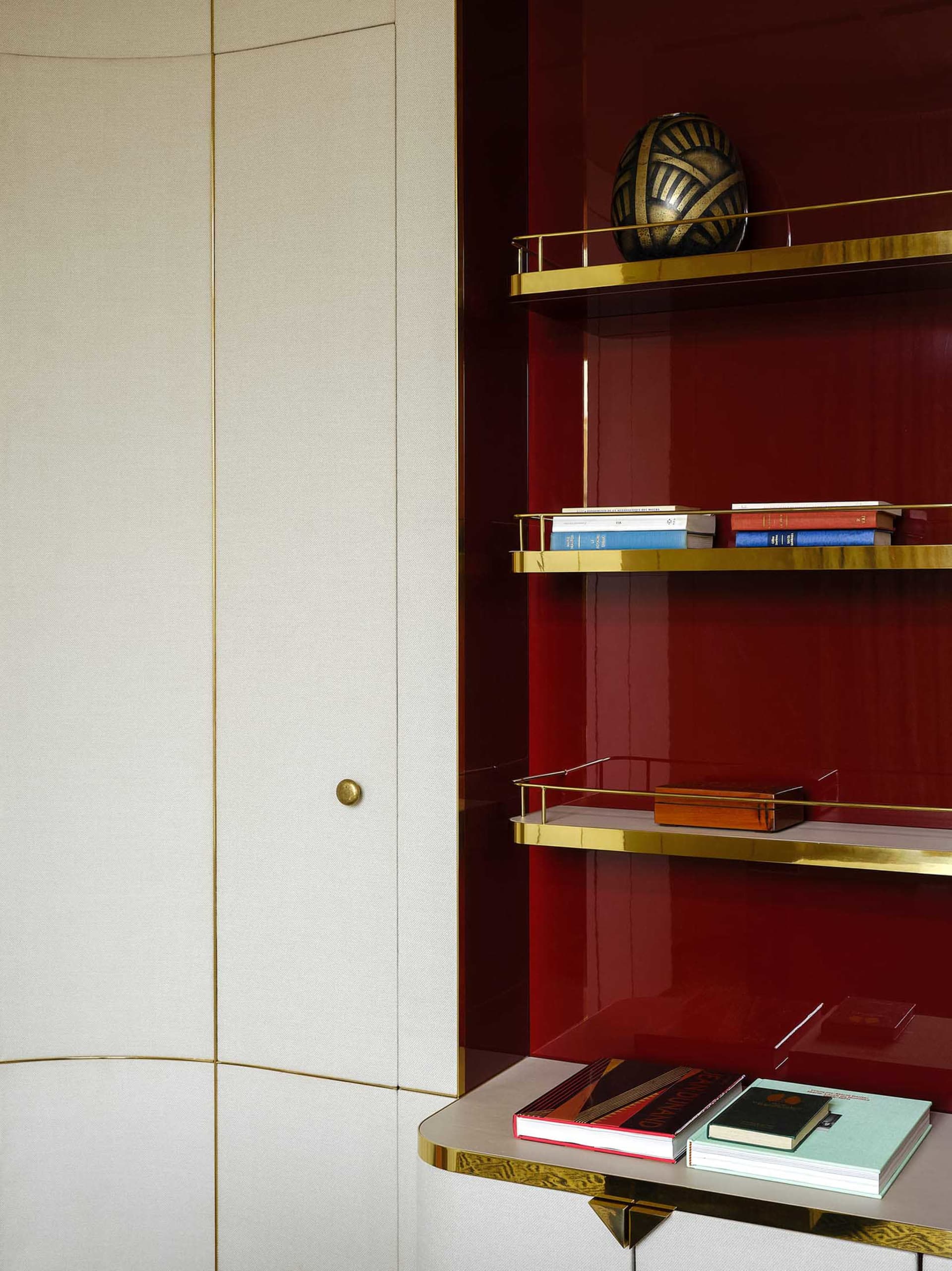 A modern, metallic brass bookshelf with gold accents, featuring a red wall and books.
