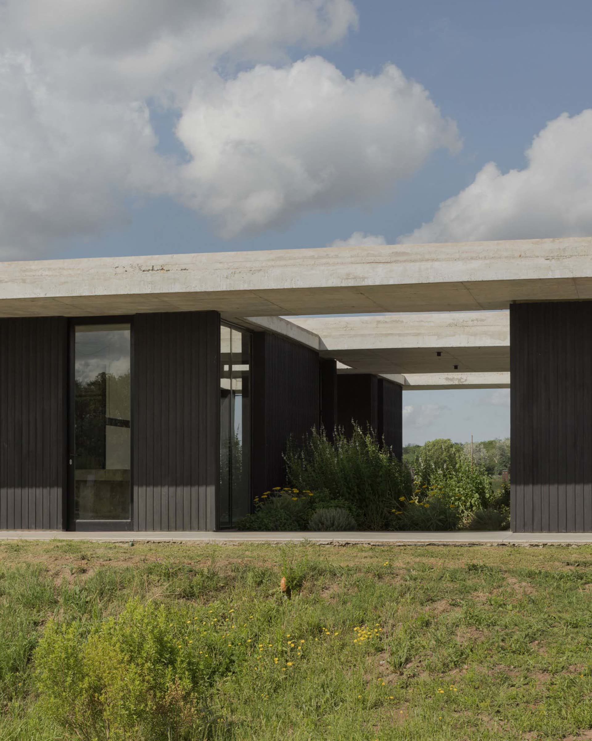 Modern residential exterior featuring concrete pillars and dark panels with glass doors.