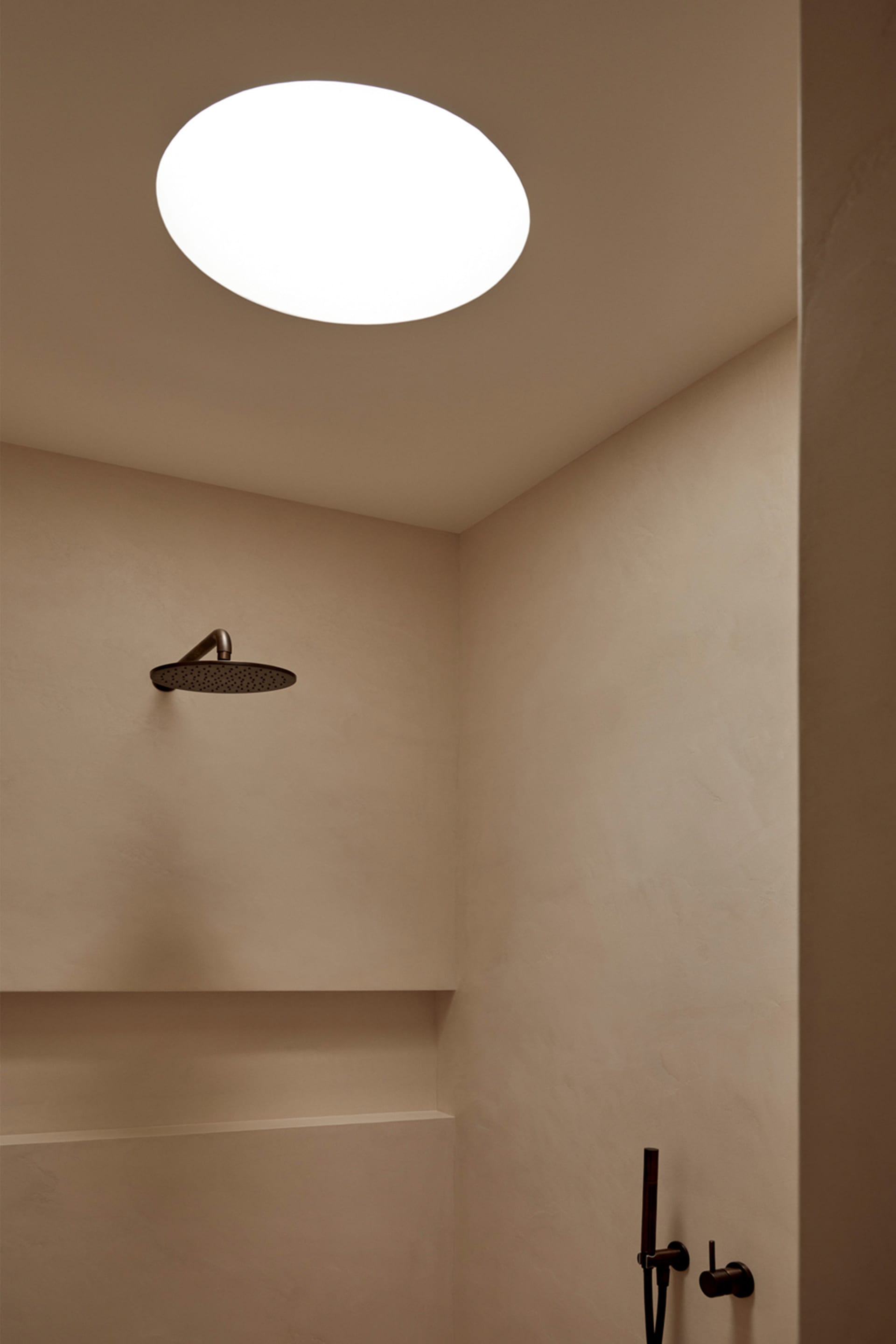 A minimalist bathroom with a round skylight and a minimalist shower fixture.