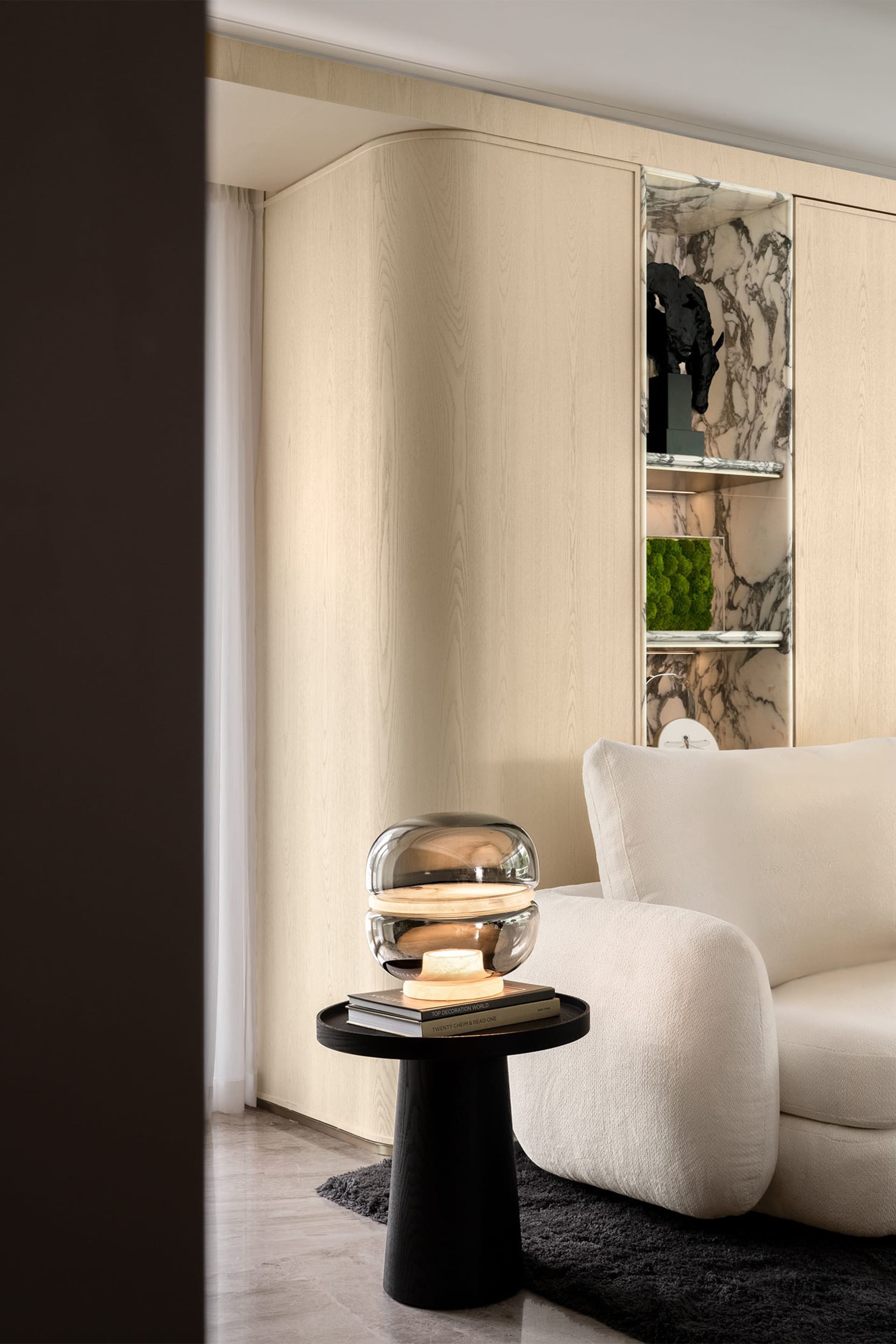 A modern living room with minimalist furniture, a sleek lamp, and a wall-mounted shelf displaying decorative items.