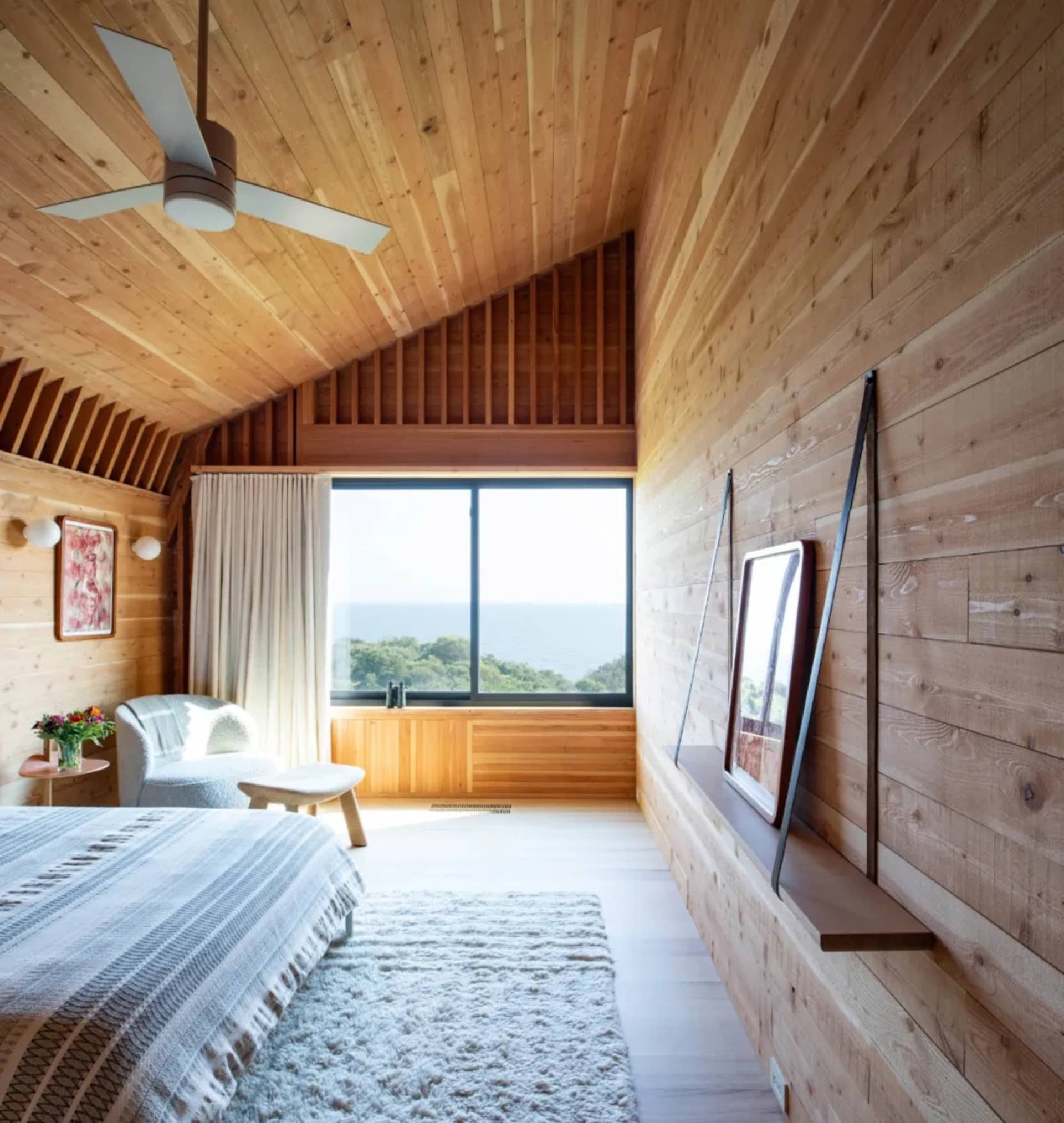 A minimalist bedroom featuring wood paneling, a large window with a view, and a cozy seating area.