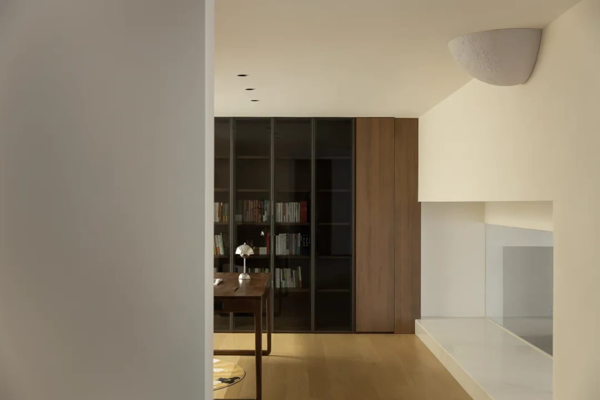 A minimalist modern office space with wooden floors, glass cabinets, and a desk setup.