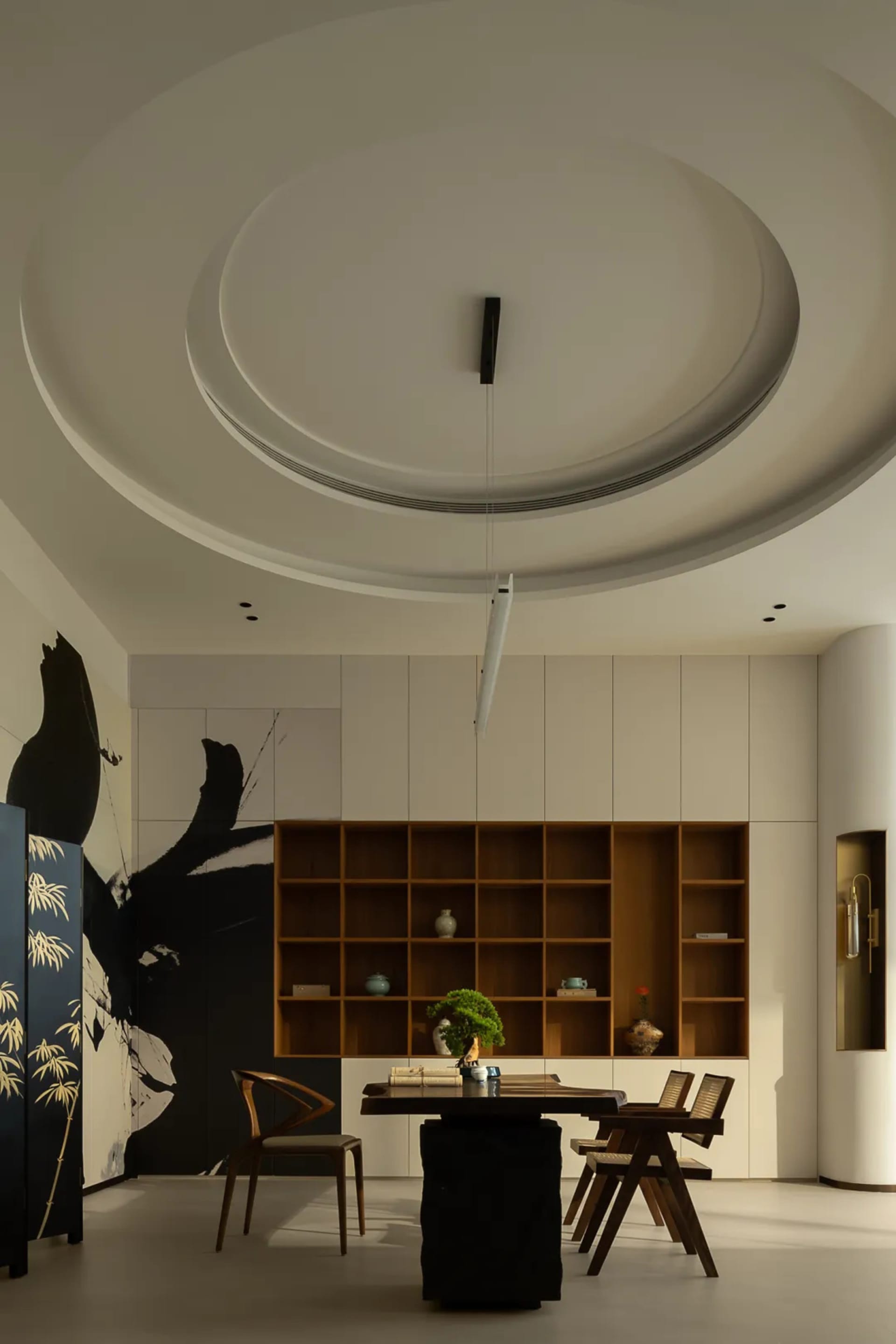 A modern home library space with a sleek, minimalist design featuring a wooden bookshelf, a black pedestal table, and a hangi