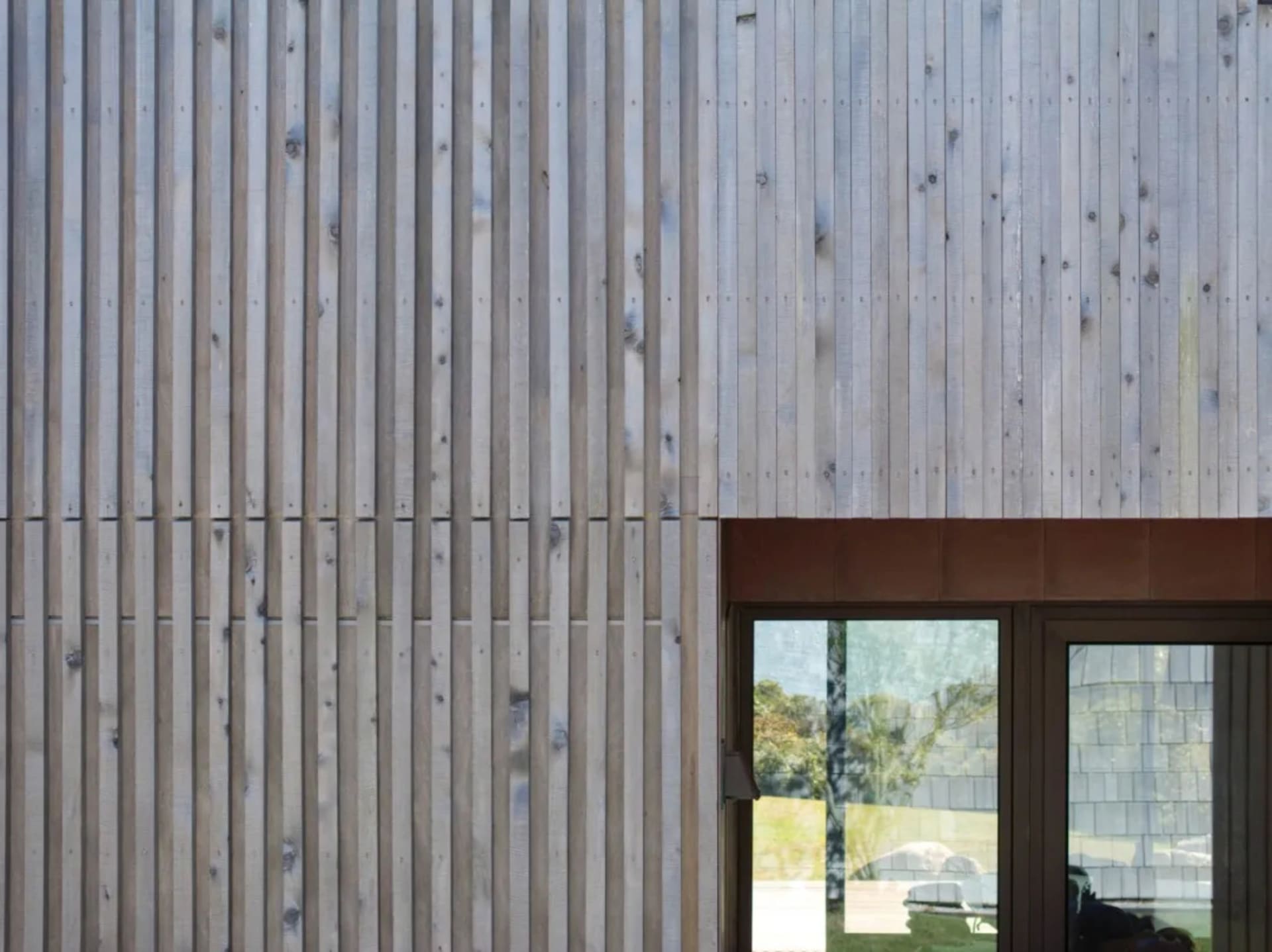 Modern house exterior clad in wooden panels with large glass doors.