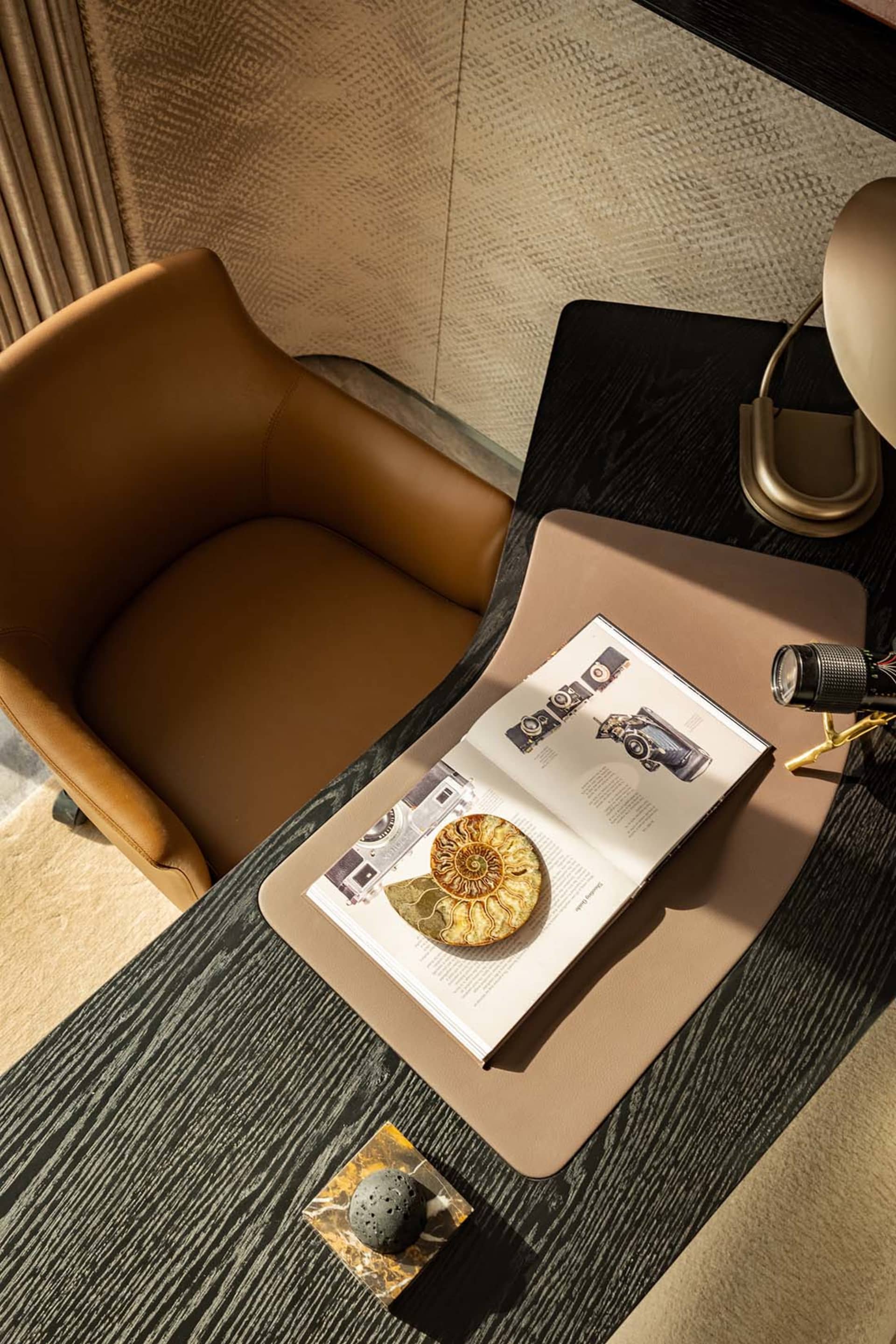 A modern, minimalist home office desk made of wood with a leather chair, a book, and a decorative ammonite化石放在上面,背景墙是纹理材质。