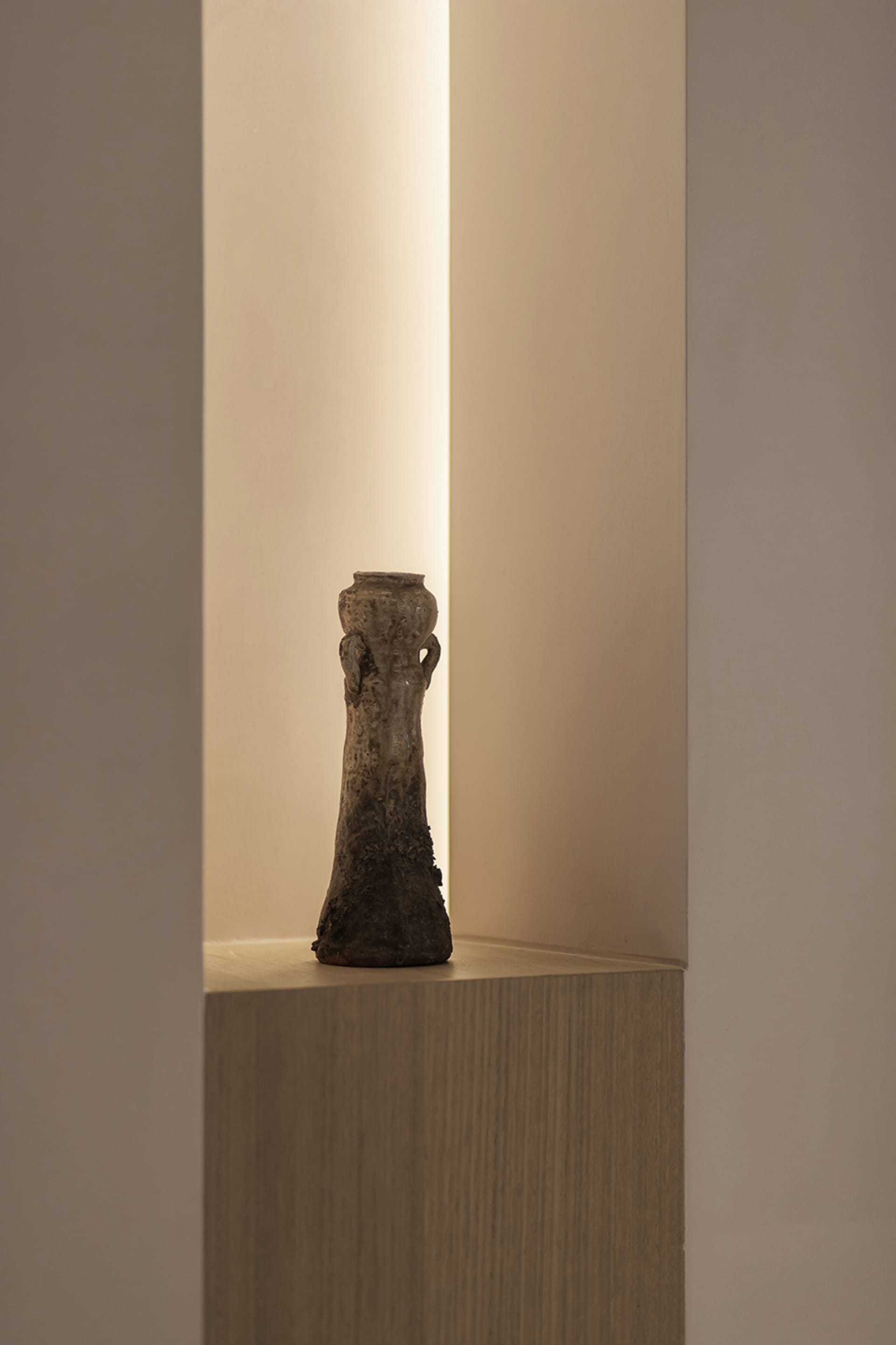 A ceramic vase with an industrial style design sits on a wooden pedestal in a minimalist setting.