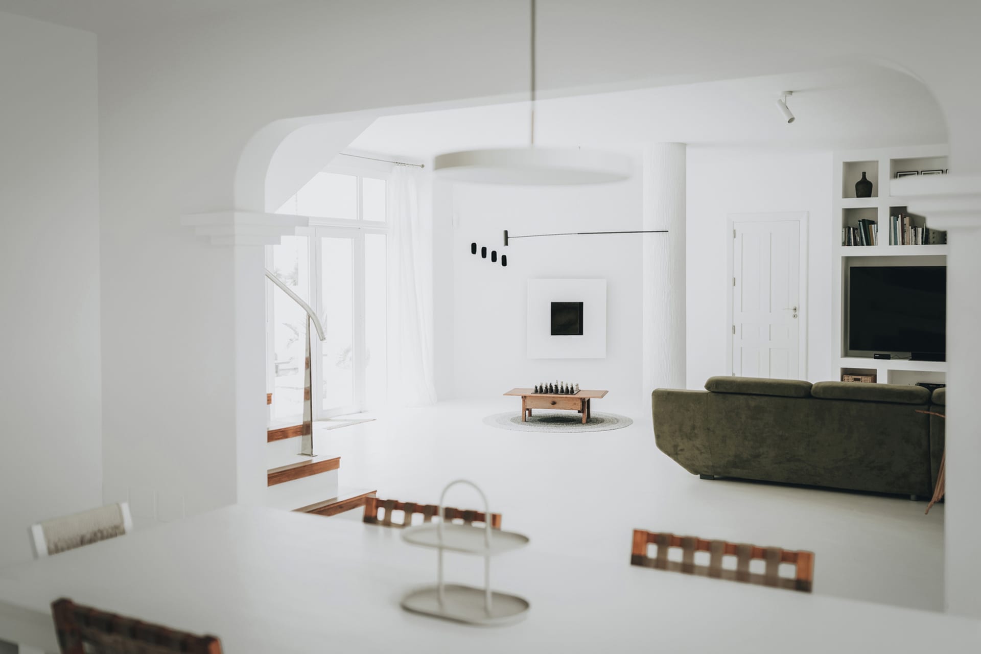 A minimalist living room featuring white tiles, a green sofa, and a modern coffee table with chess pieces.