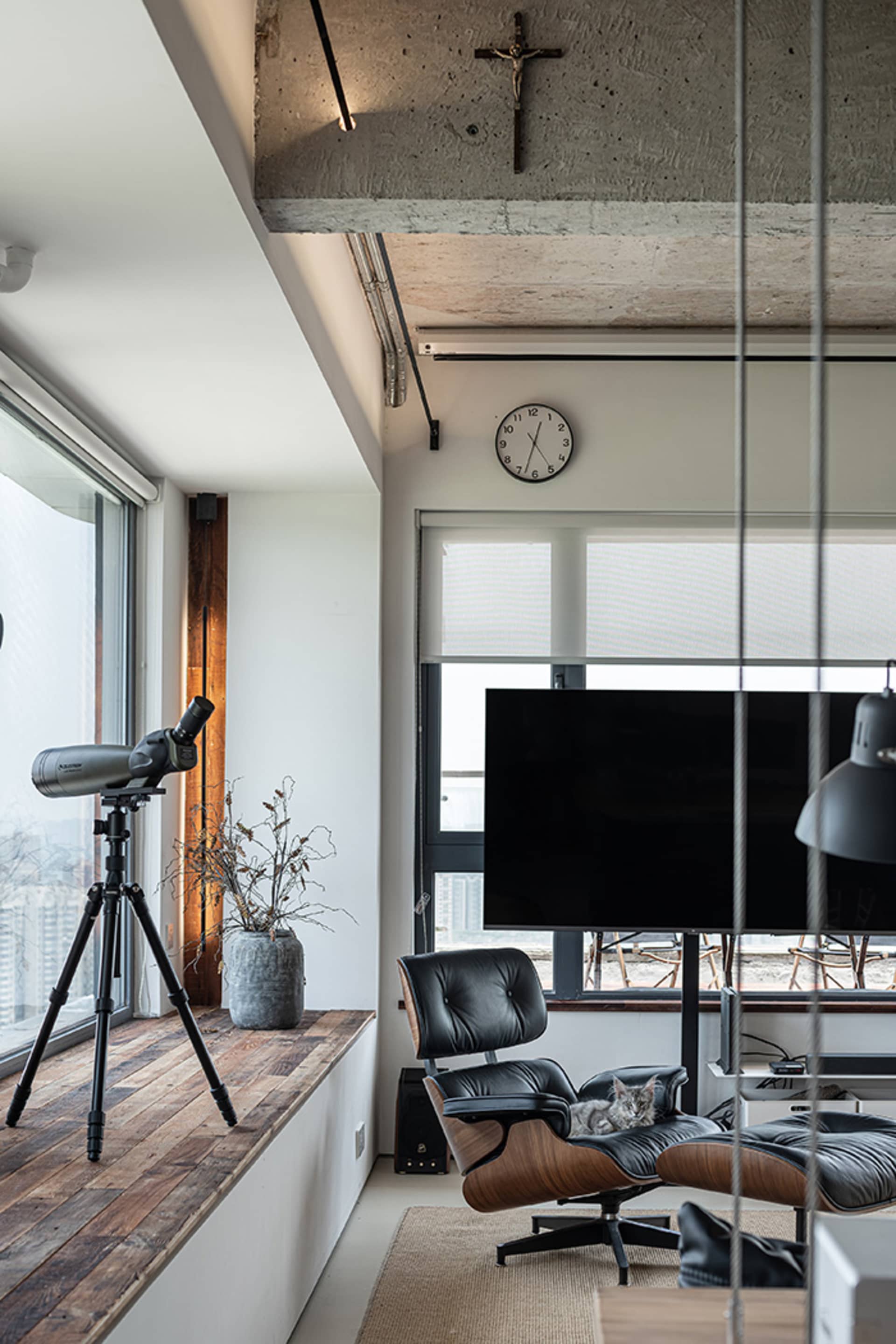 Modern living room with a sleek leather chair, a wall-mounted television, a tripod-mounted telescope, and a crucifix hanging