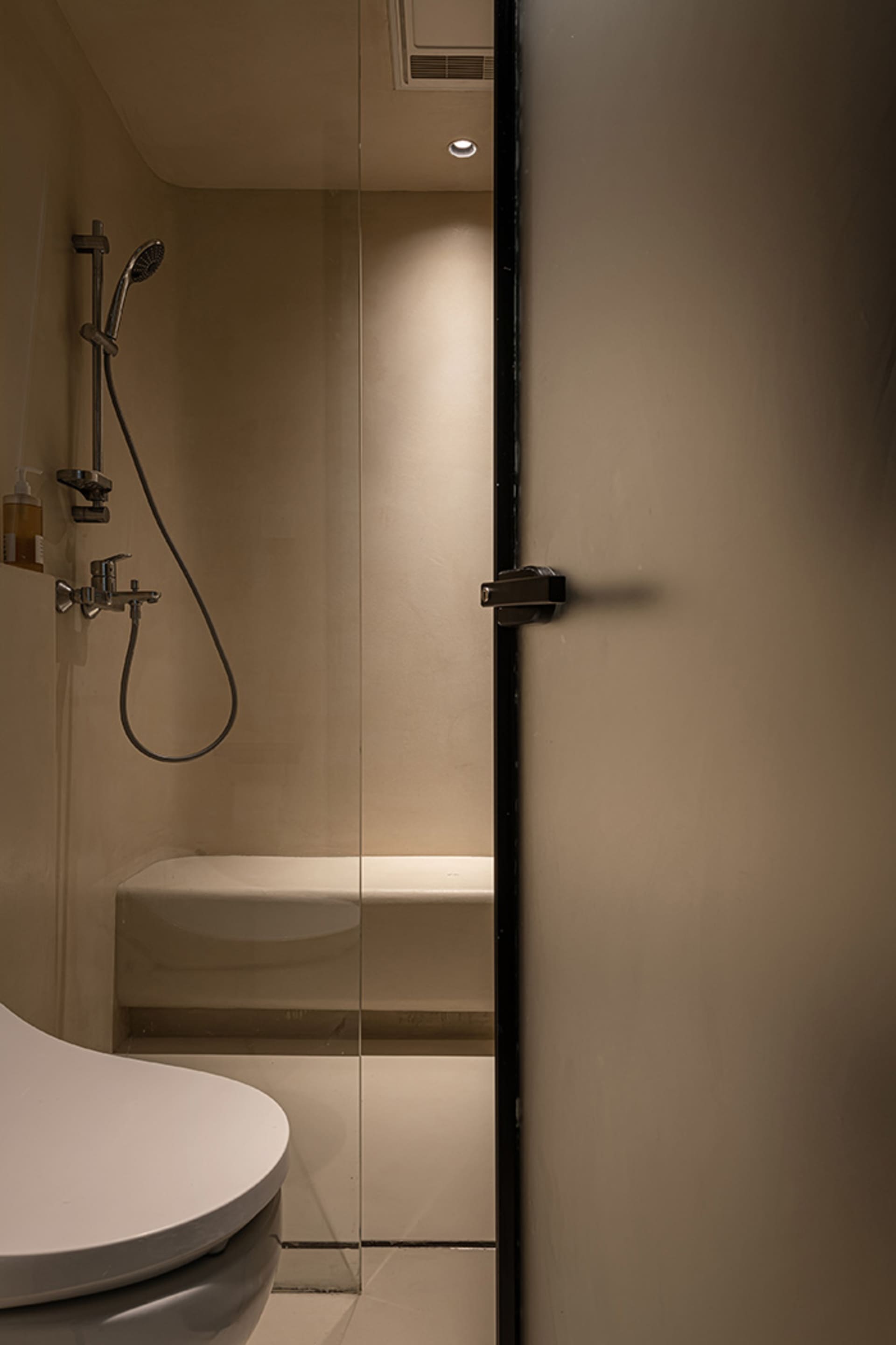 Modern minimalist bathroom with concrete walls and floor, featuring a white toilet and a glass shower enclosure with a handhe