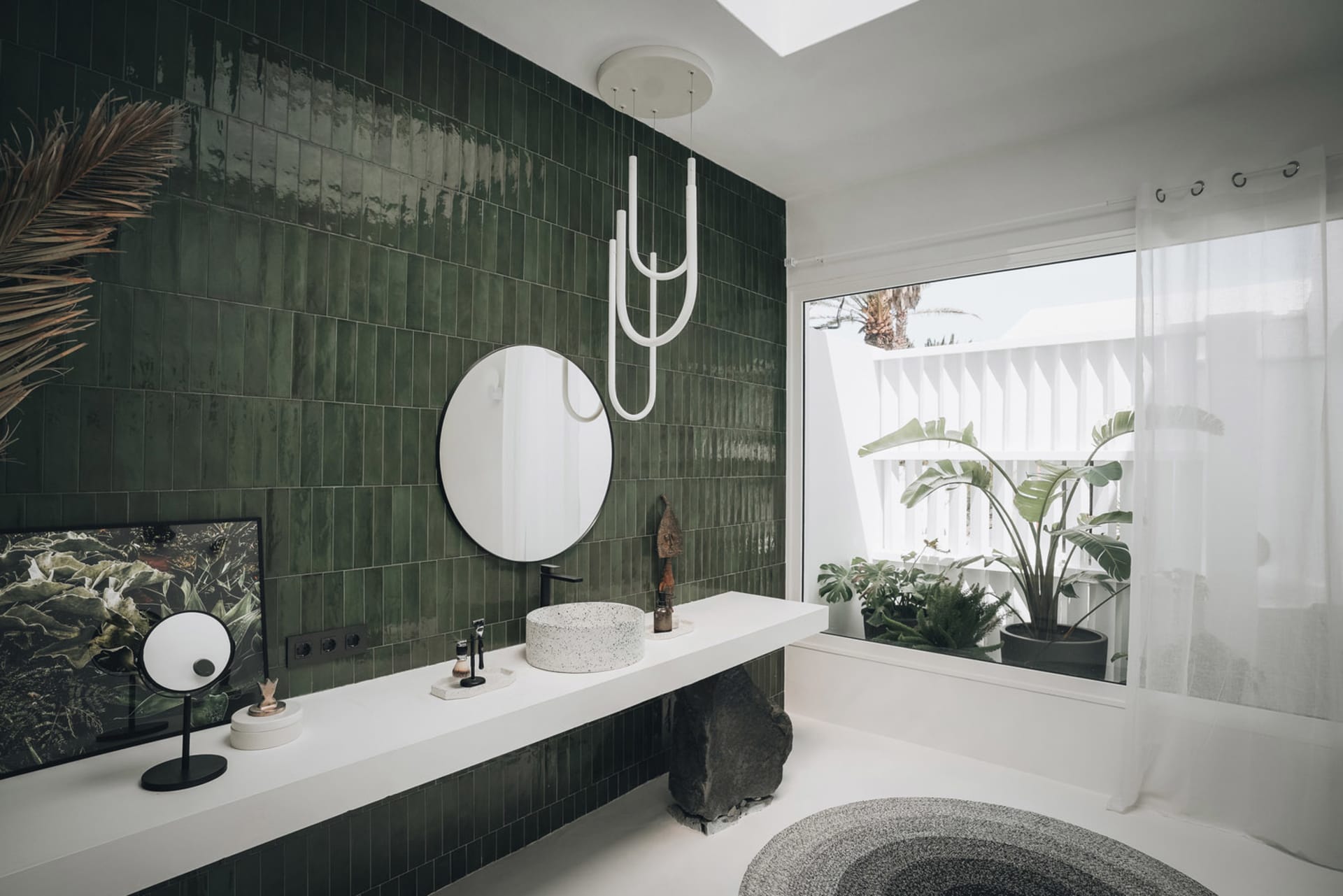 A modern minimalist bathroom featuring green tiles, a round mirror, black faucet, and a round sink.
