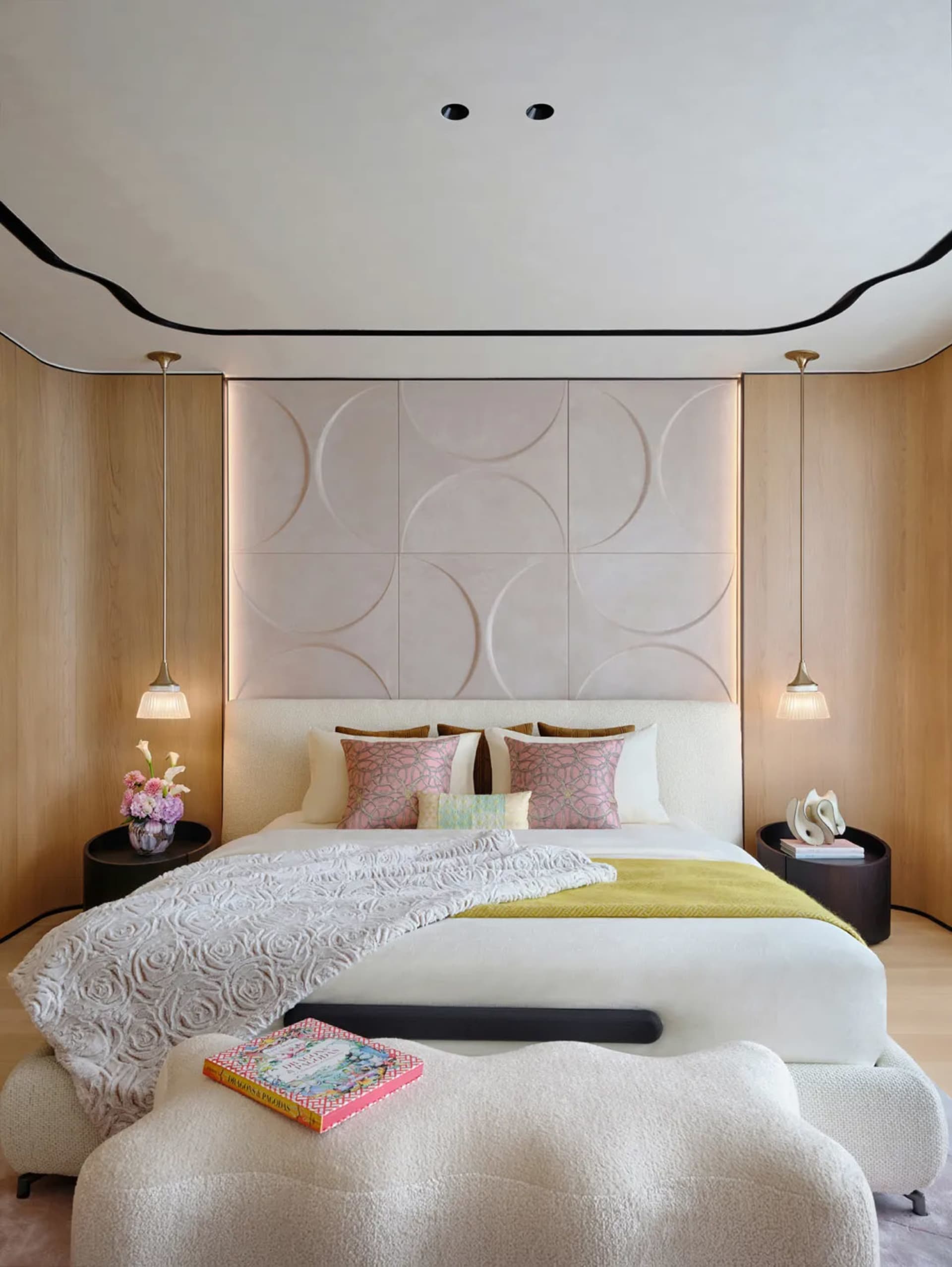 Modern bedroom with a bed adorned with pillows and blankets, featuring a wooden headboard and fabric textures.